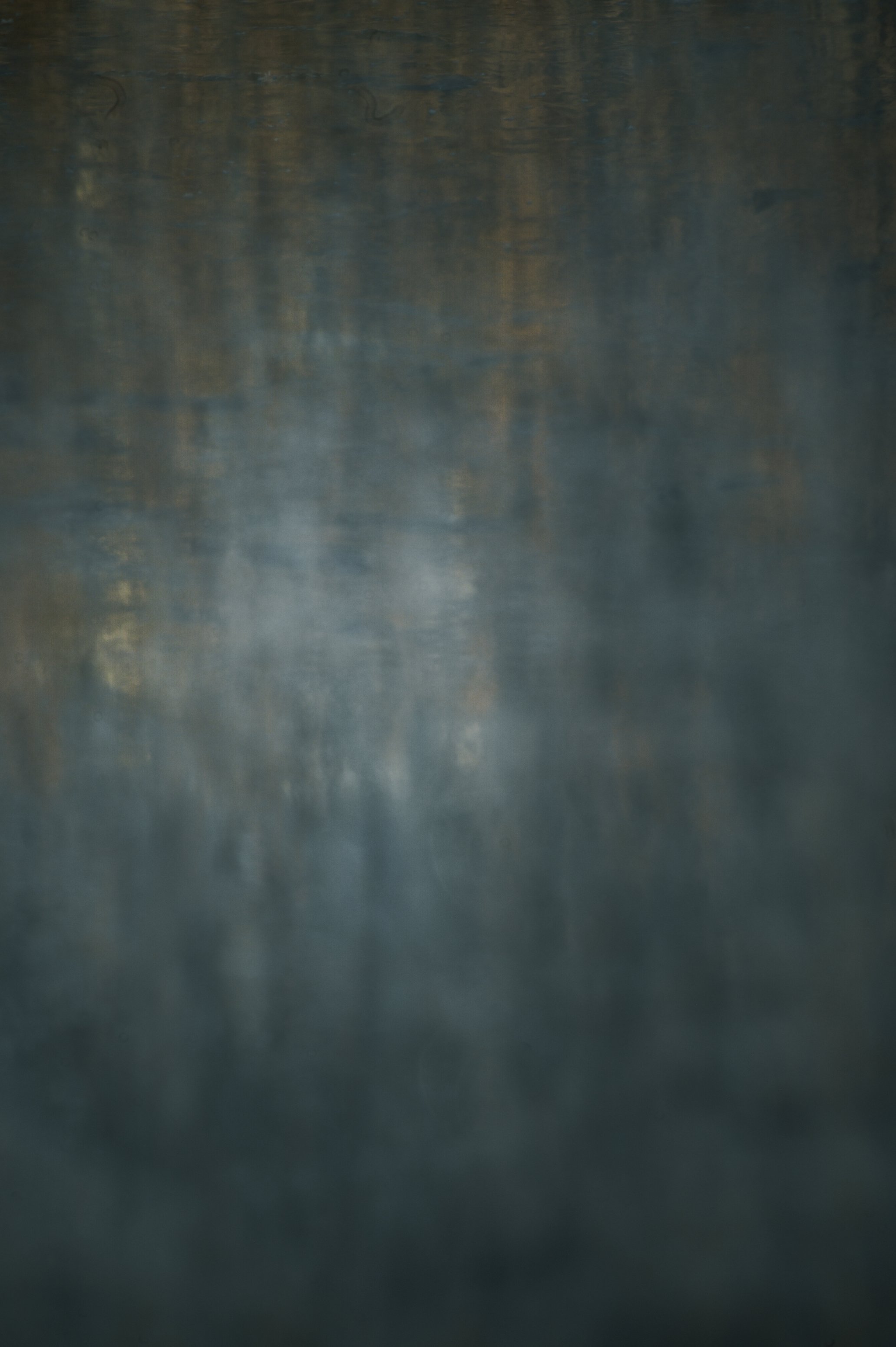 Das Bild zeigt eine dunkle, neblige Wasseroberfläche, die spiegelt und eine ruhige, mystische Atmosphäre schafft.