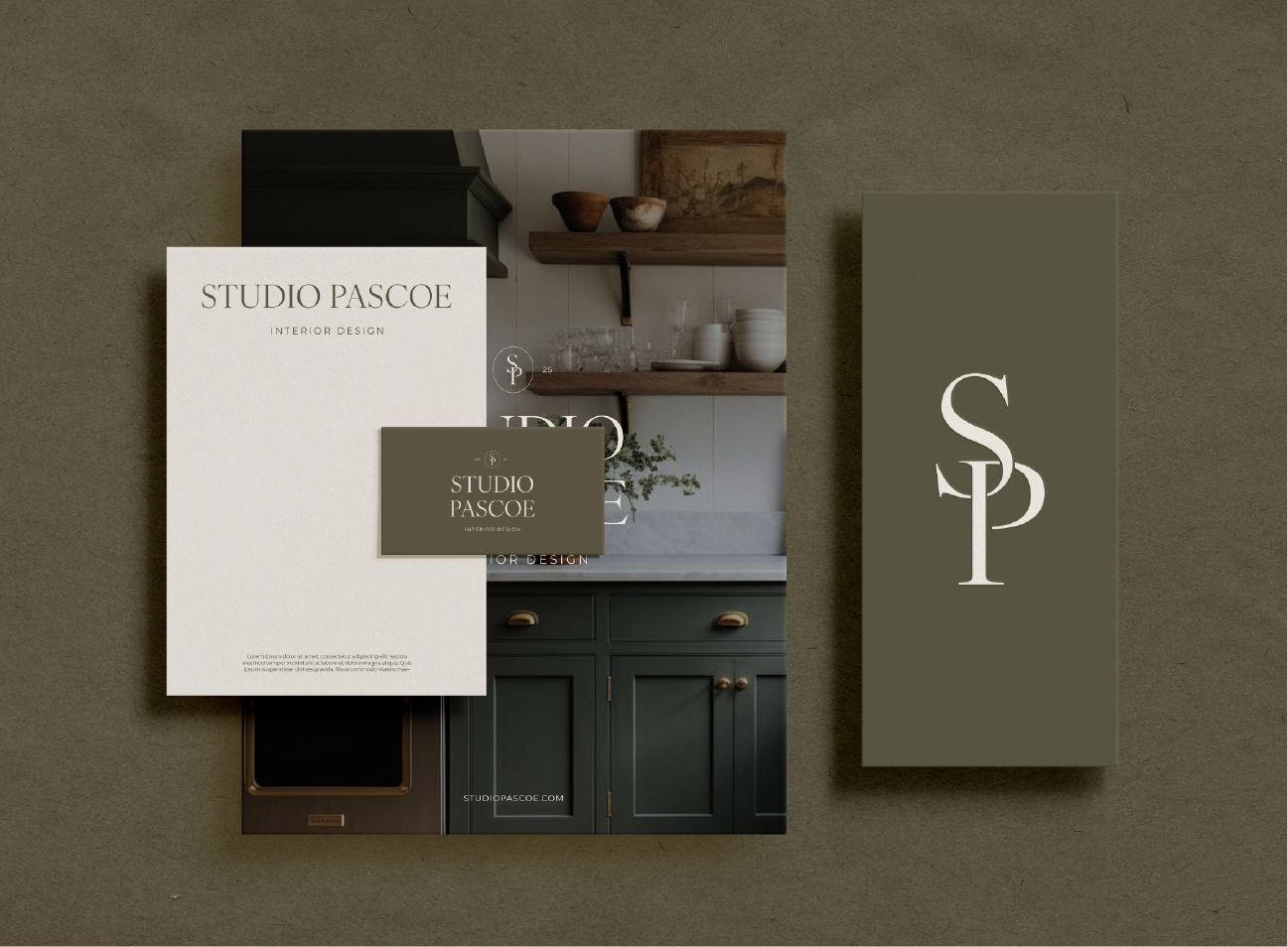 Business branding materials for Studio Pascoe interior design, including a brochure, business card, and a large sign with the logo and website, displayed on a textured surface.