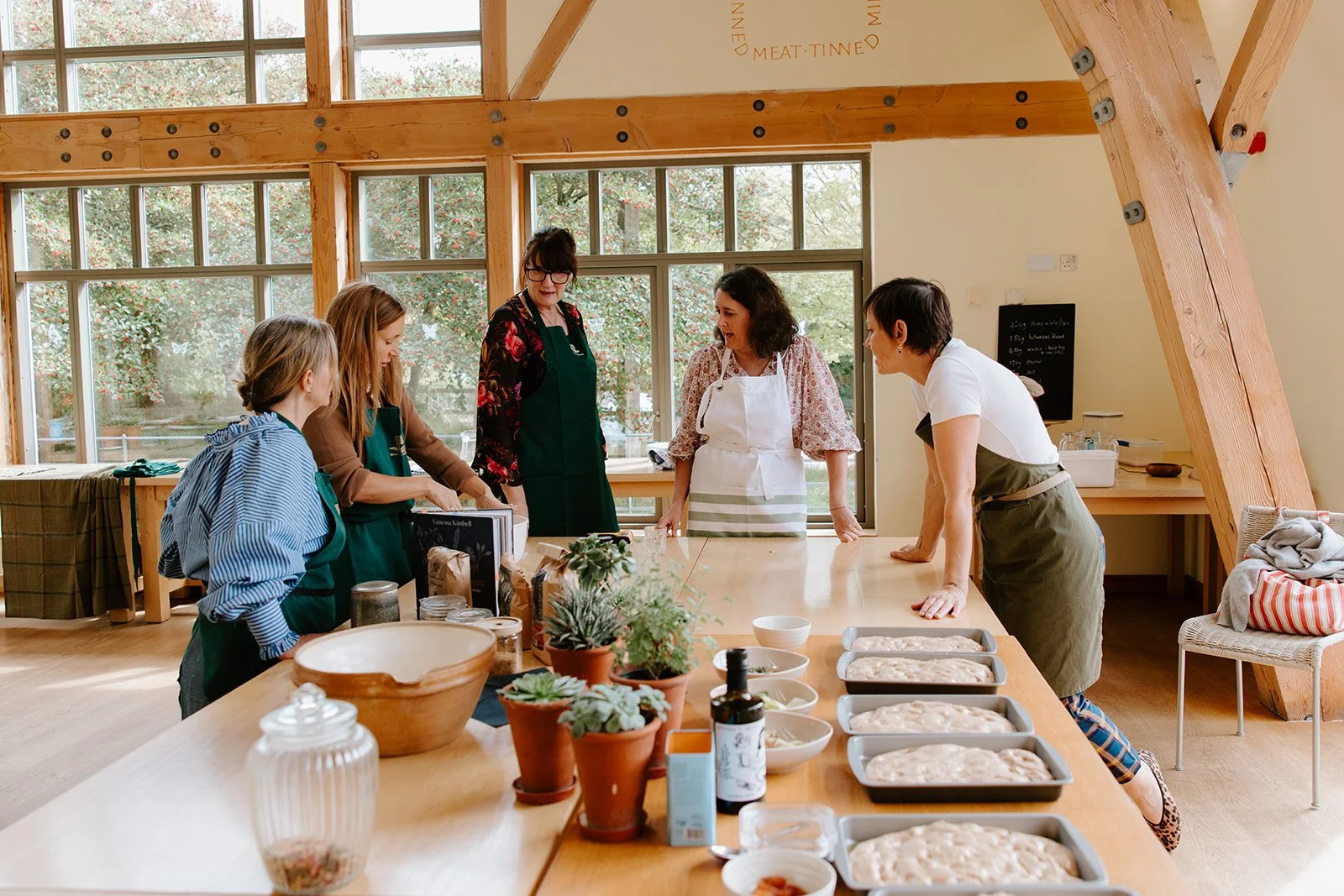 Five women gathered around a table watching a demonstration of bread making
