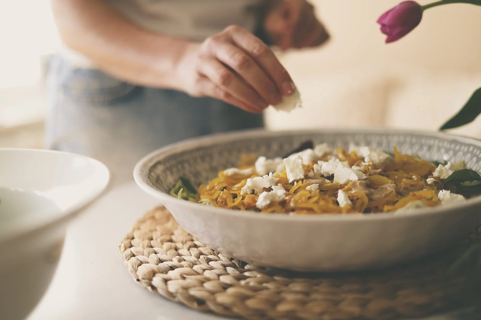 A woman crumbling feta into a large bowl containing salad.