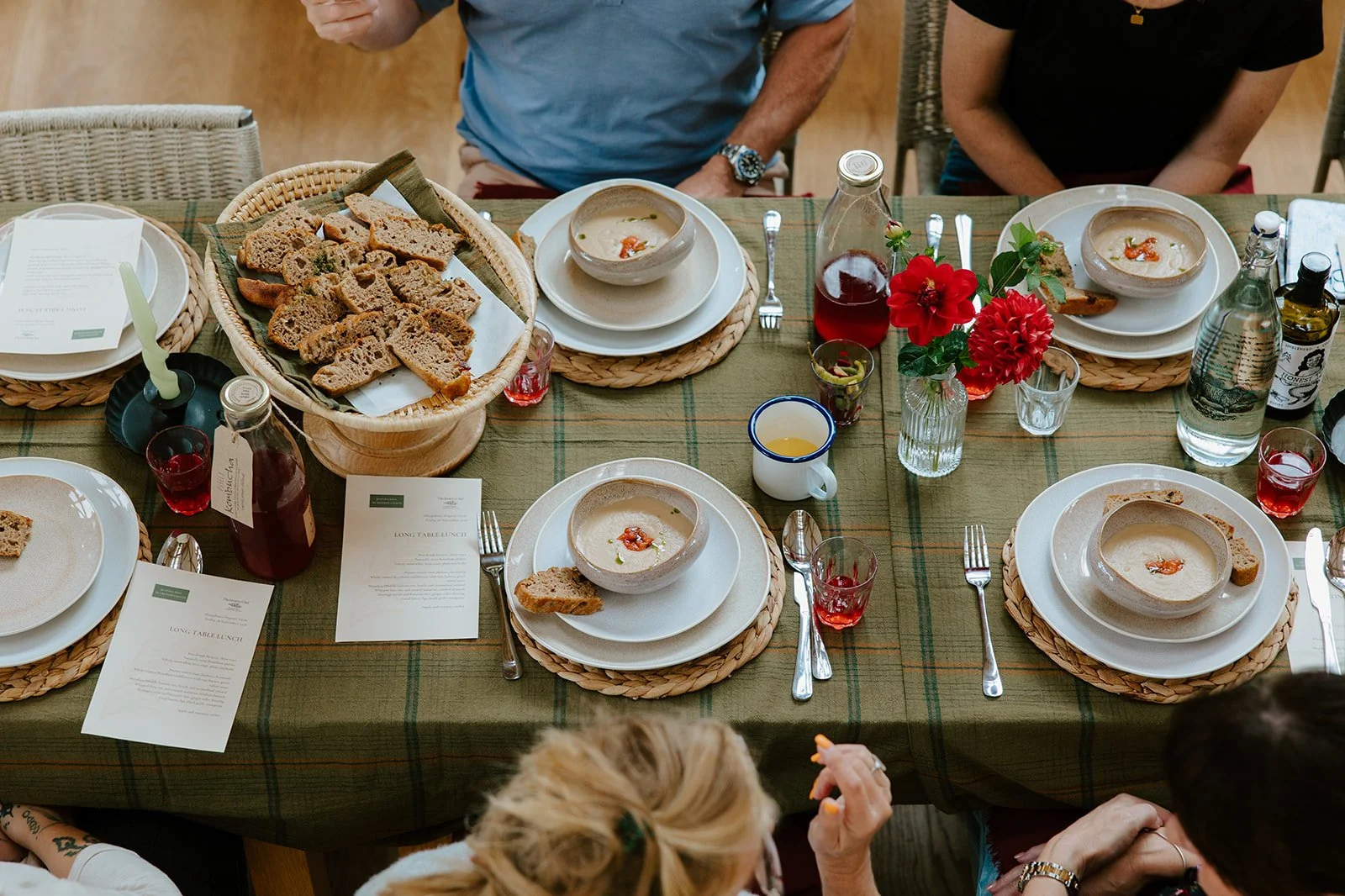 A long table lunch with bowls of soup, bread and drinks. People are sitting around the table talking.