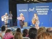 Three people on stage at the Triangular Memorial Theater, with an audience watching.