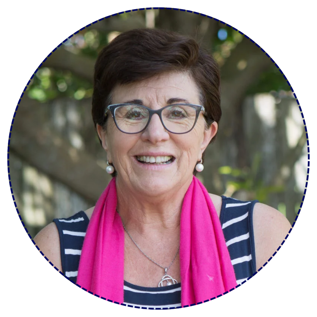 Maggie Dent a woman and parenting expert with short dark hair and glasses smiling outdoors, wearing a striped top, pink scarf, pearl earrings, and a silver necklace with a peace sign pendant.