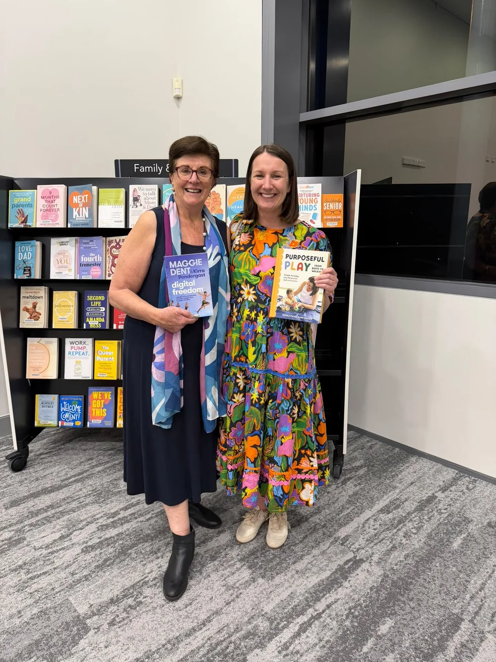 Maggie Dent and Nicole Pates smiling together in front of a book display, Maggie holding her book Digital Freedom and Nicole holding Purposeful Play