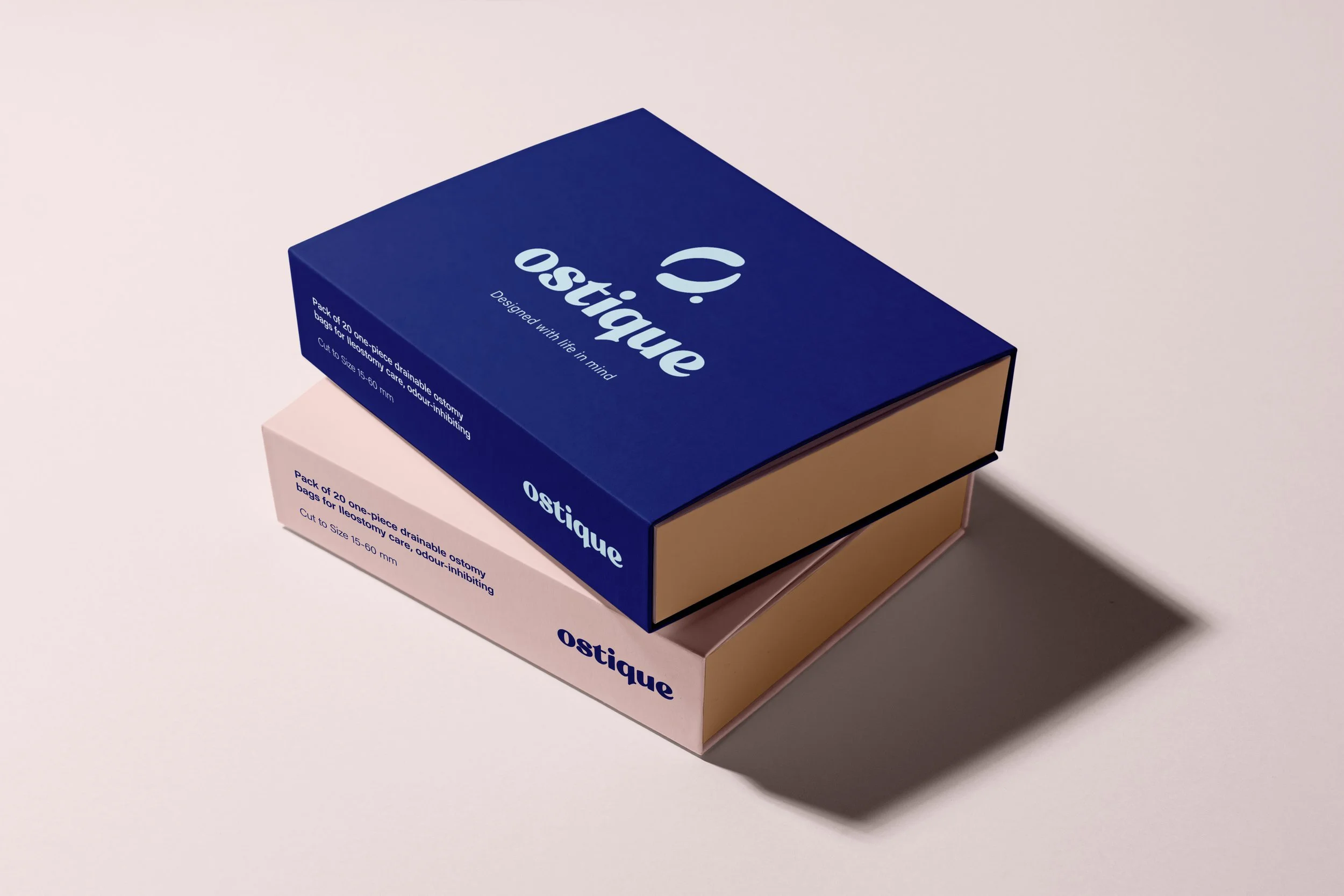 Two stacked boxes of ostique brand disposable drainable ostomy bags, one in blue on top of a light pink box, both on a light surface with soft shadow.