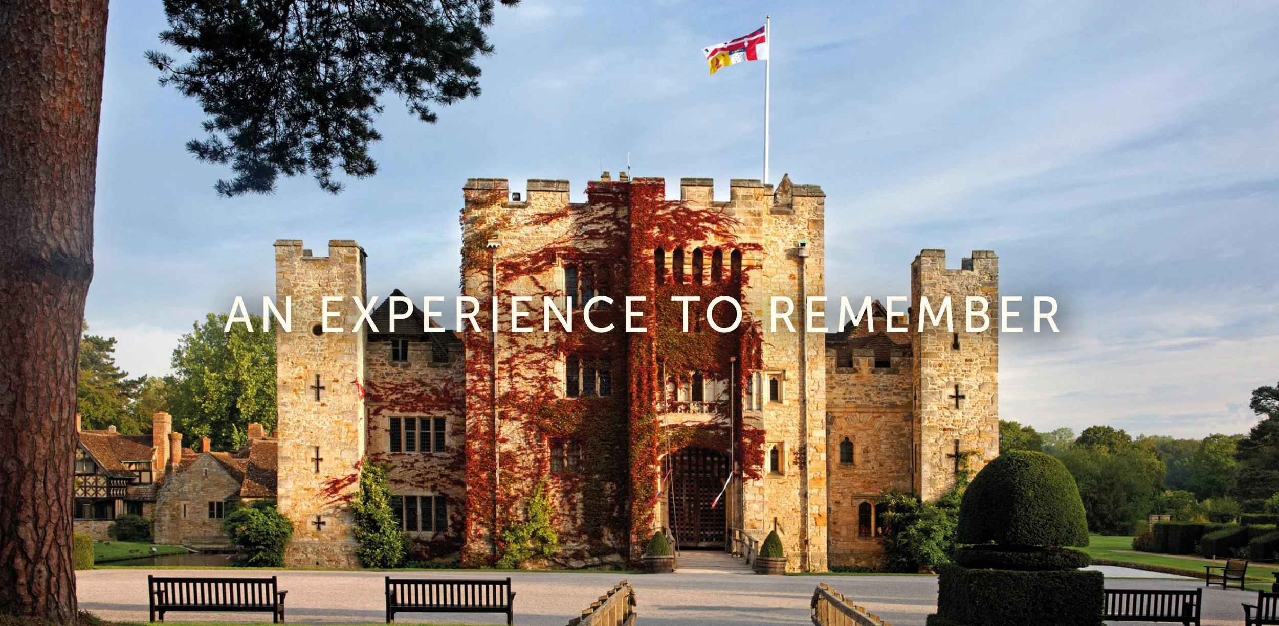 A historic stone castle with ivy-covered walls, surrounded by a park with trees, benches, and manicured bushes, under a partly cloudy sky. Text overlay reads 'An Experience to Remember.'
