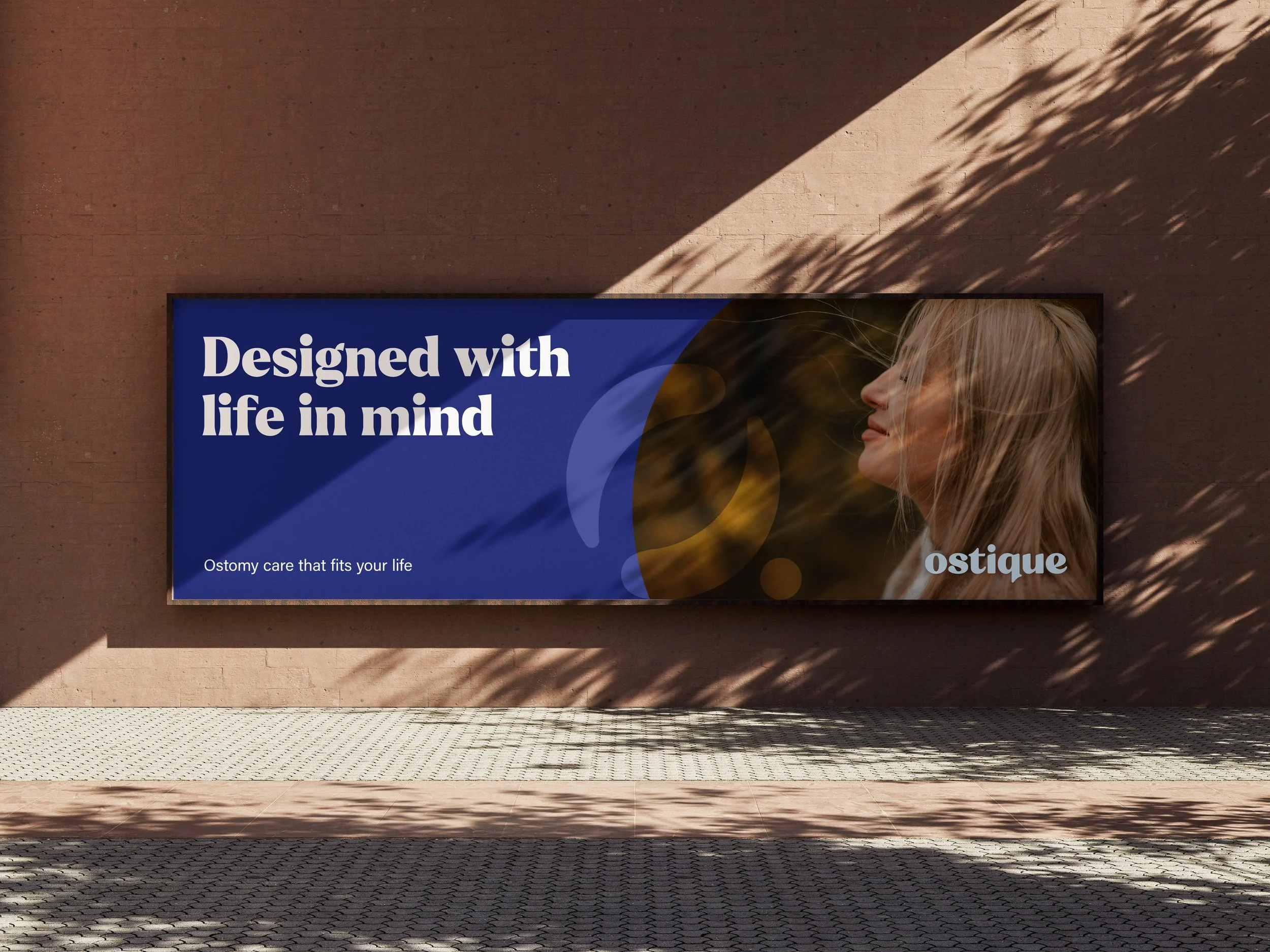 Digital billboard displaying the message 'Designed with life in mind' against a pink brick wall, with sunlight and shadows creating a pattern on the wall and billboard.