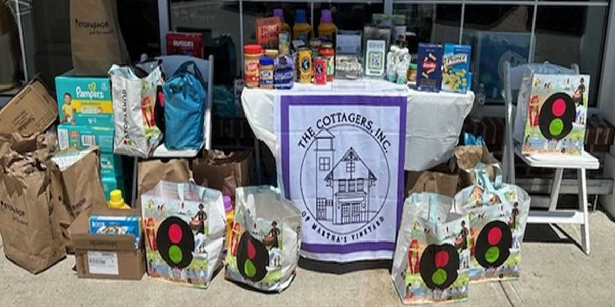 A charity display with bags and boxes of supplies, a table with various food and donations, and a sign for The Cottagers Inc. at an outdoor or indoor event.
