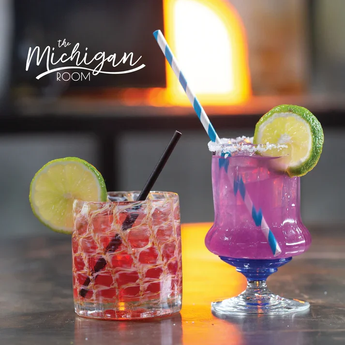 Two colorful cocktails with lime slices and striped straws on a bar counter at The Michigan Room