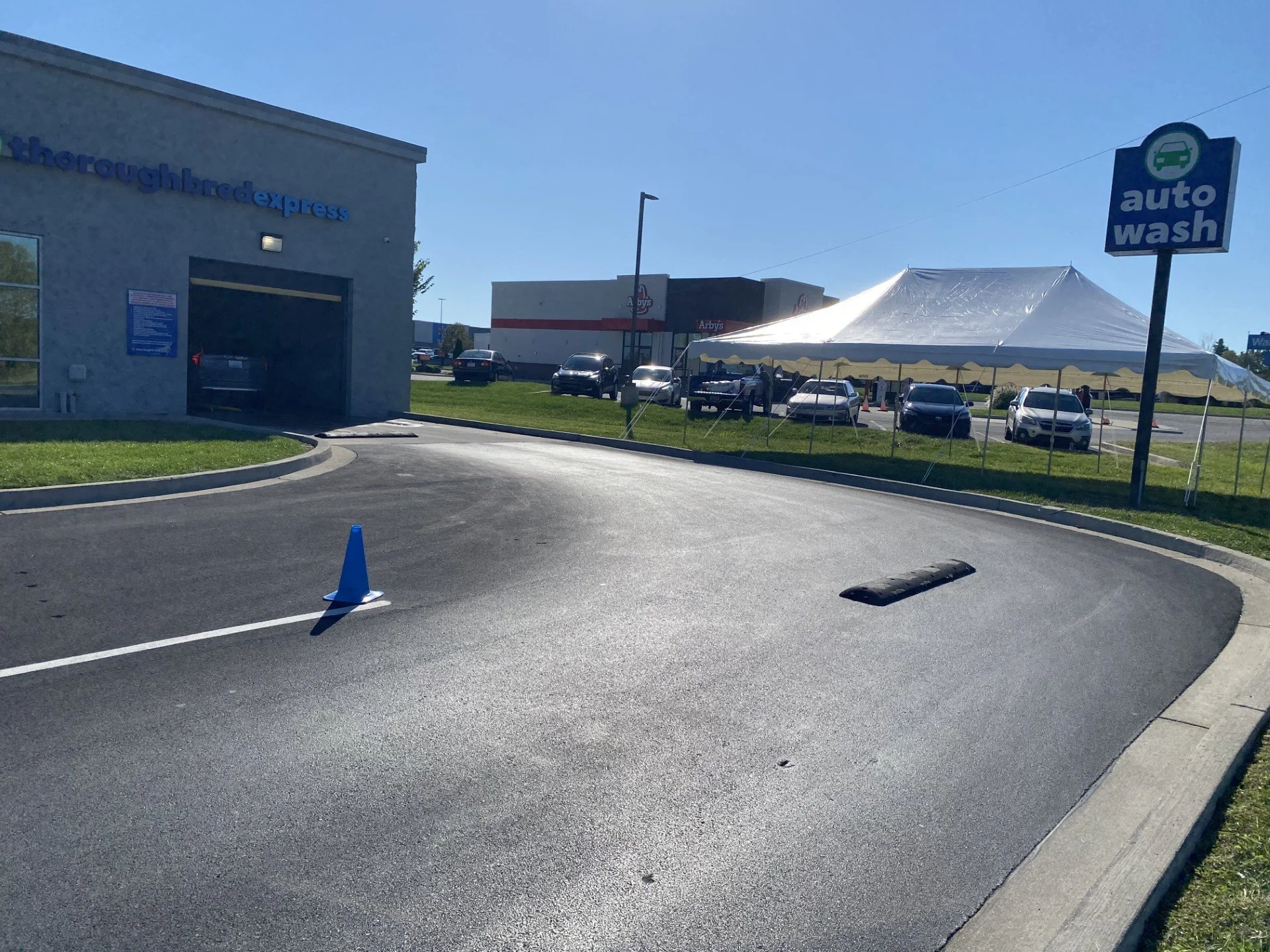 Auto wash sign outside a car wash area with a tent and parked cars under a clear blue sky.