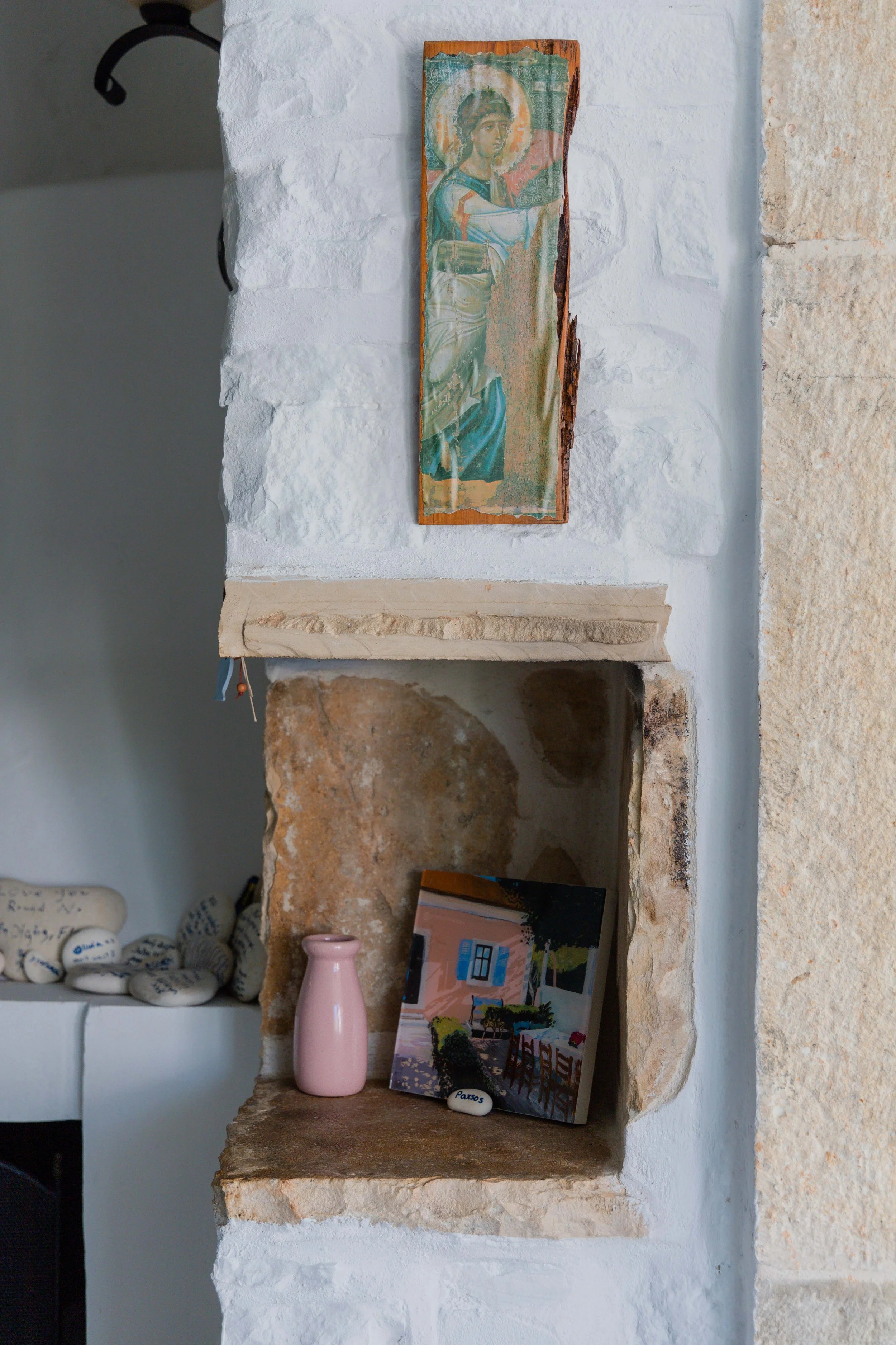 Decorative wall niche with a religious icon, pink vase, colorful painting, and small rocks with writing on them.