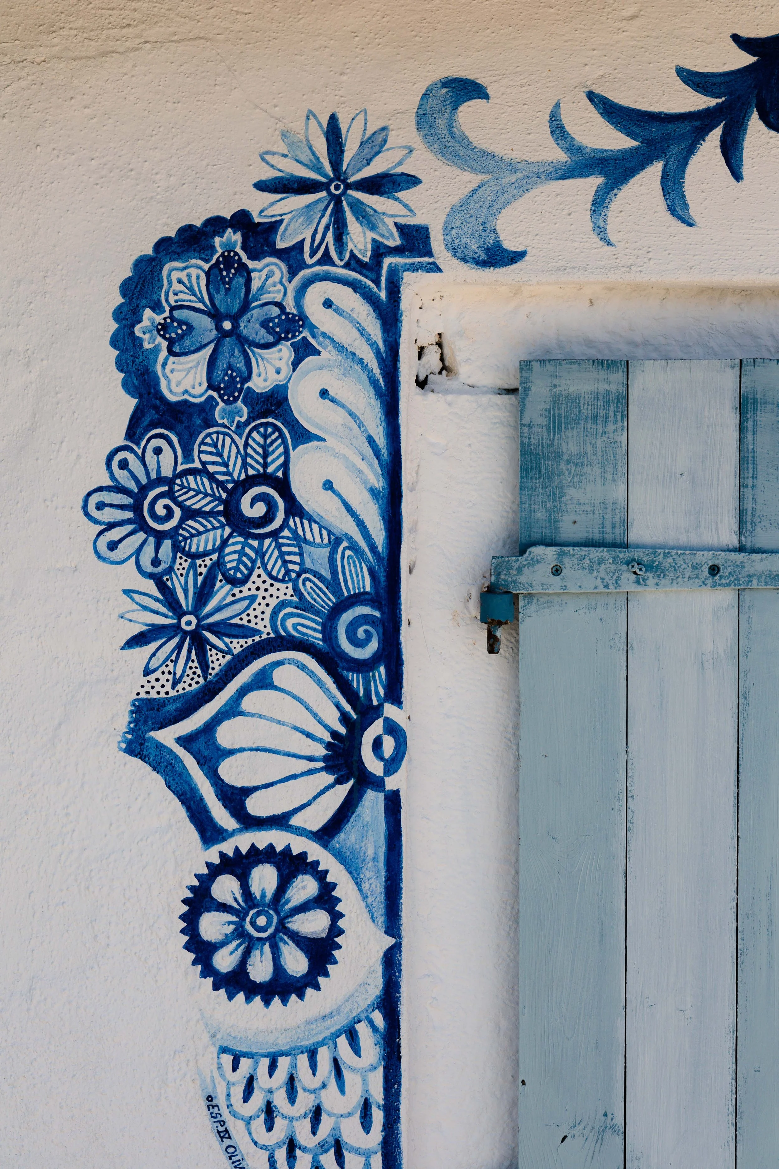 Blue floral and butterfly mural painted on a white textured wall next to a light blue wooden shutter.