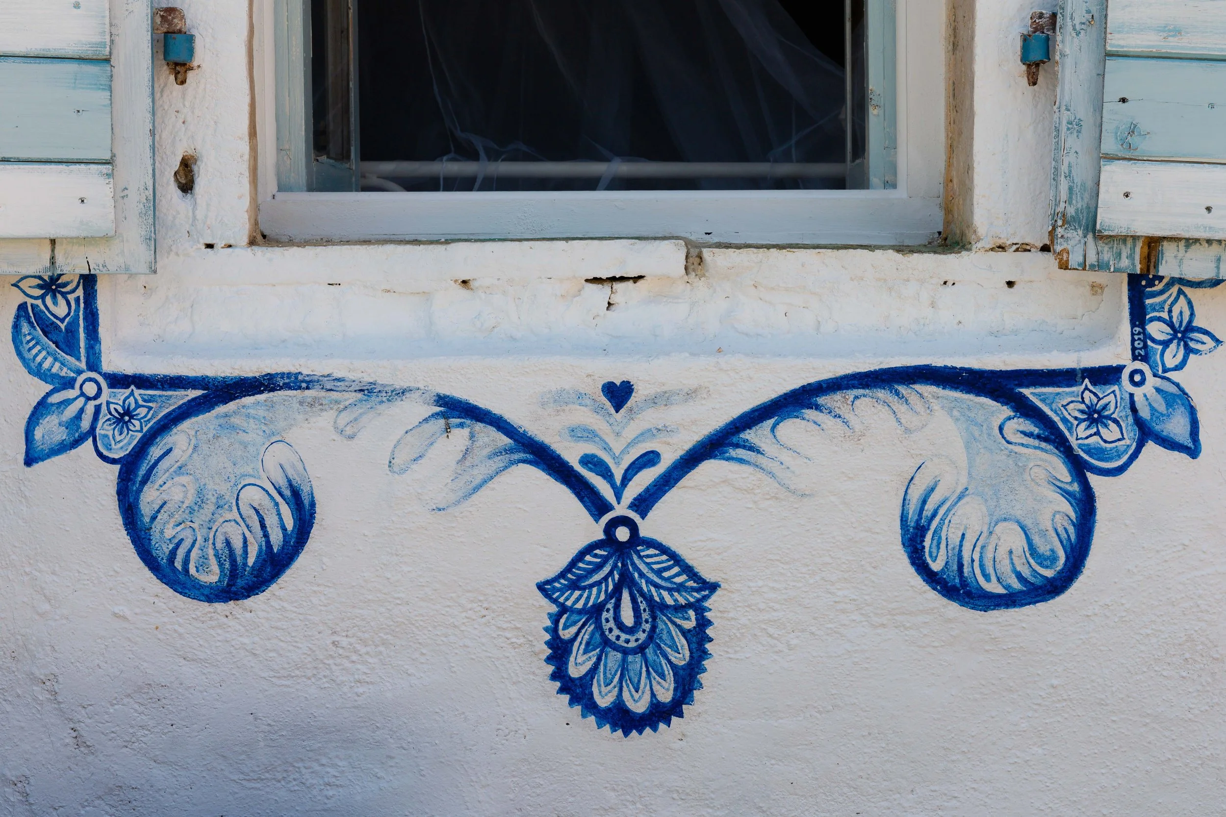 Blue painted floral design under a windowsill on a white wall.