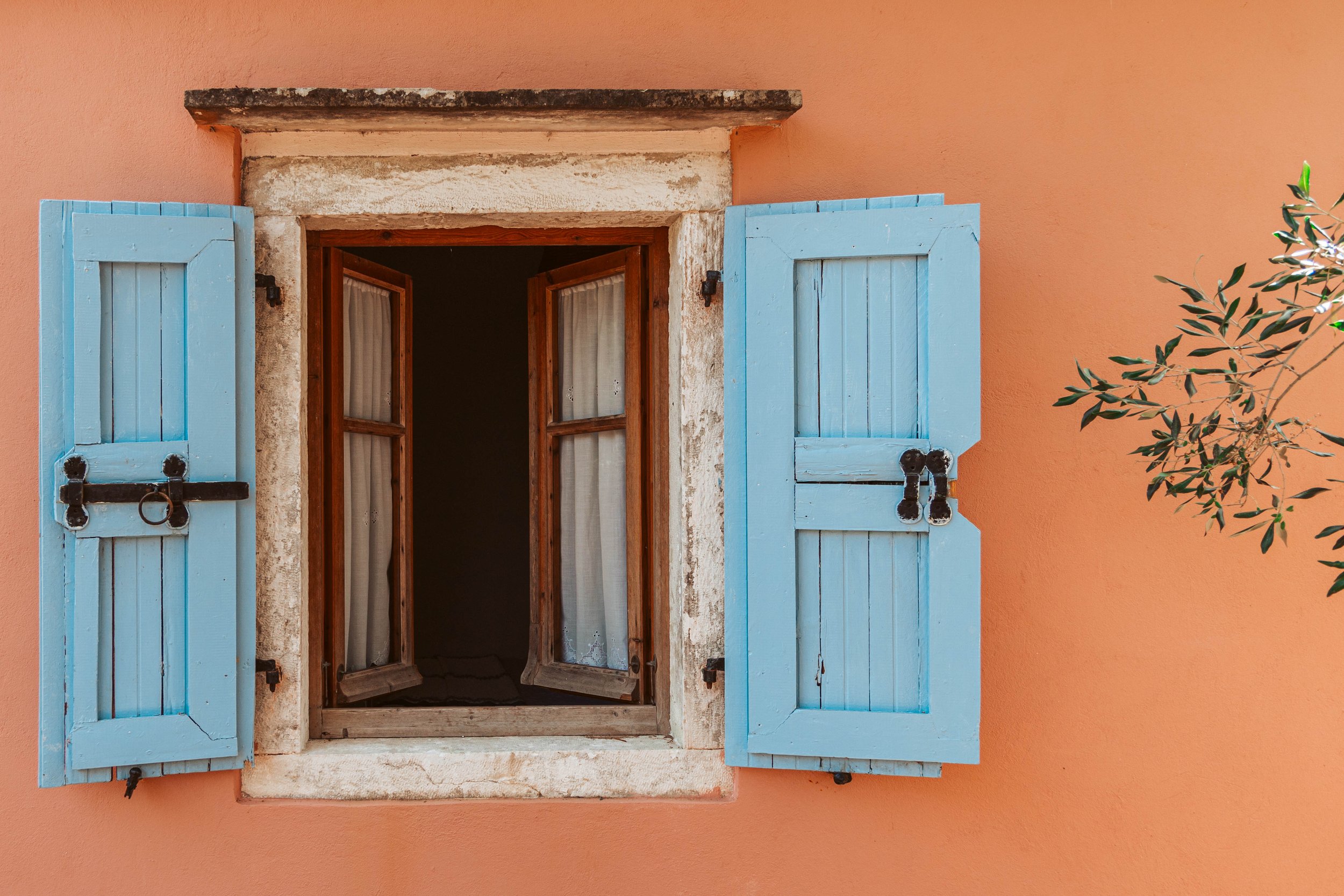 Open wooden window shutters painted light blue on an orange stucco wall.