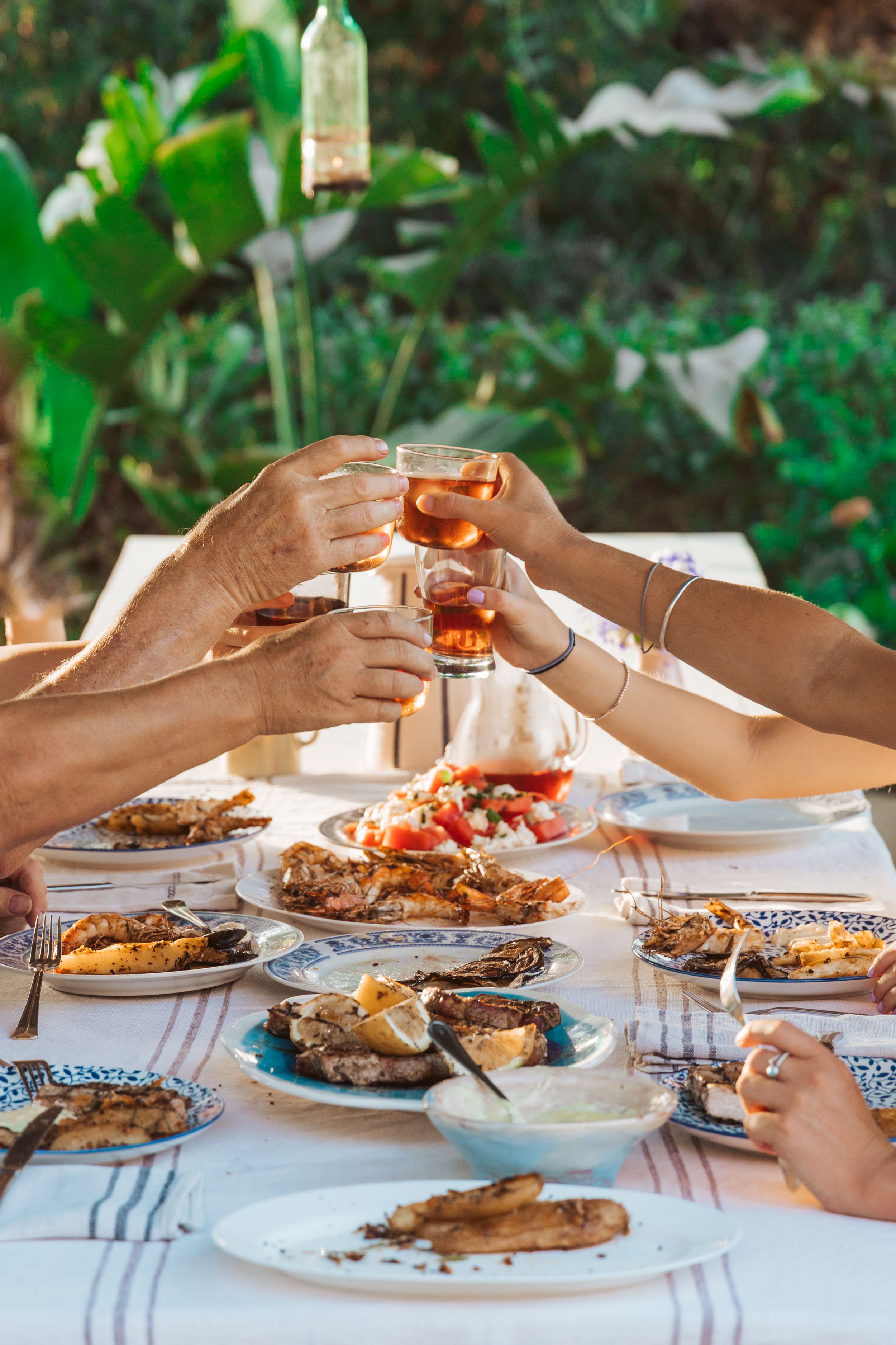 People toasting with glasses of rosé wine at an outdoor dinner table filled with various dishes, including grilled meats and salads.