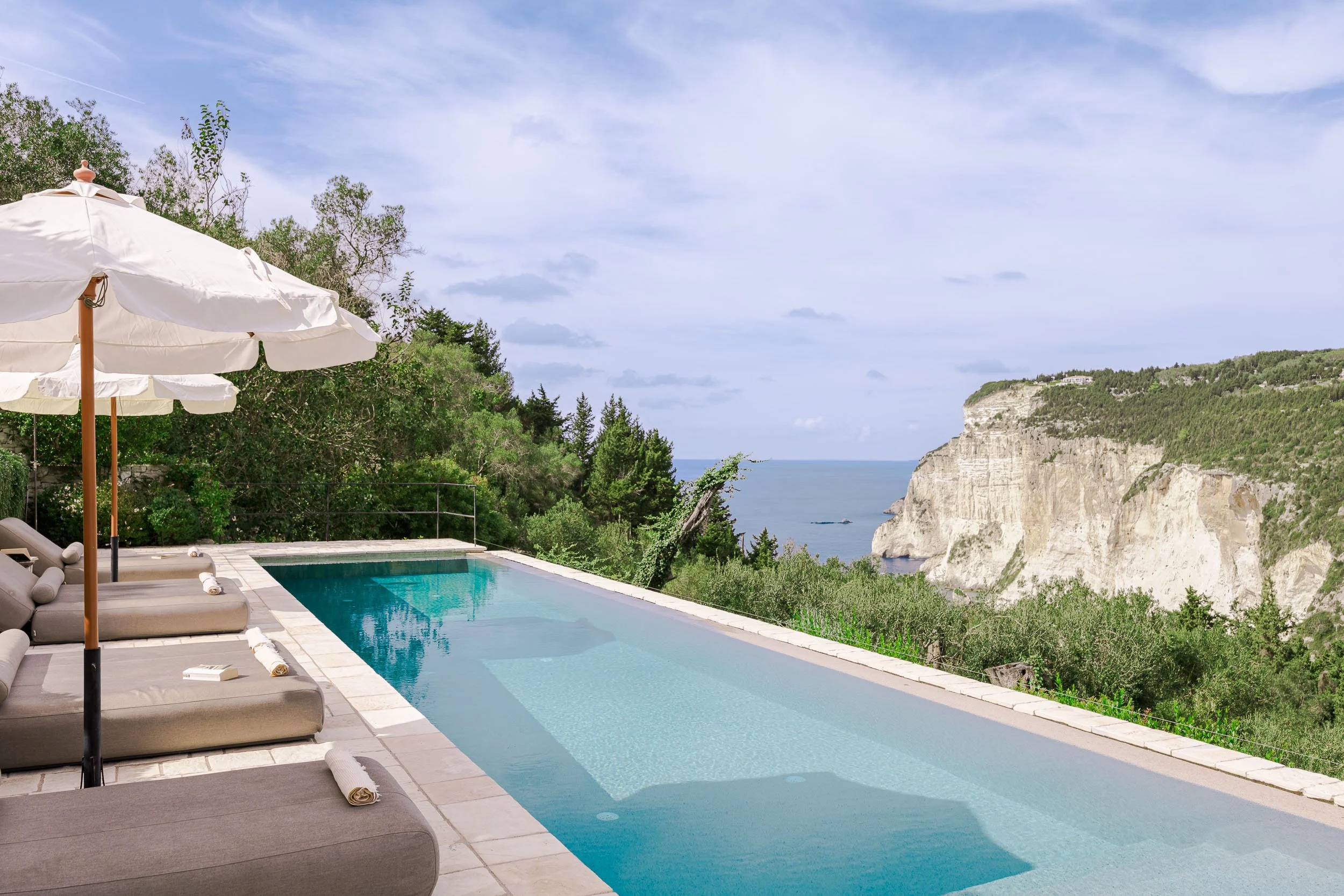 Swimming pool with lounge chairs and umbrellas overlooking cliffs and the ocean.