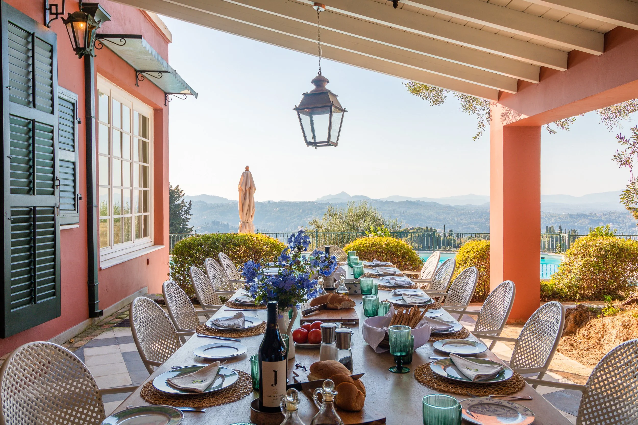 An outdoor dining table set for a meal on a patio with a scenic view of hills and sky in the background.