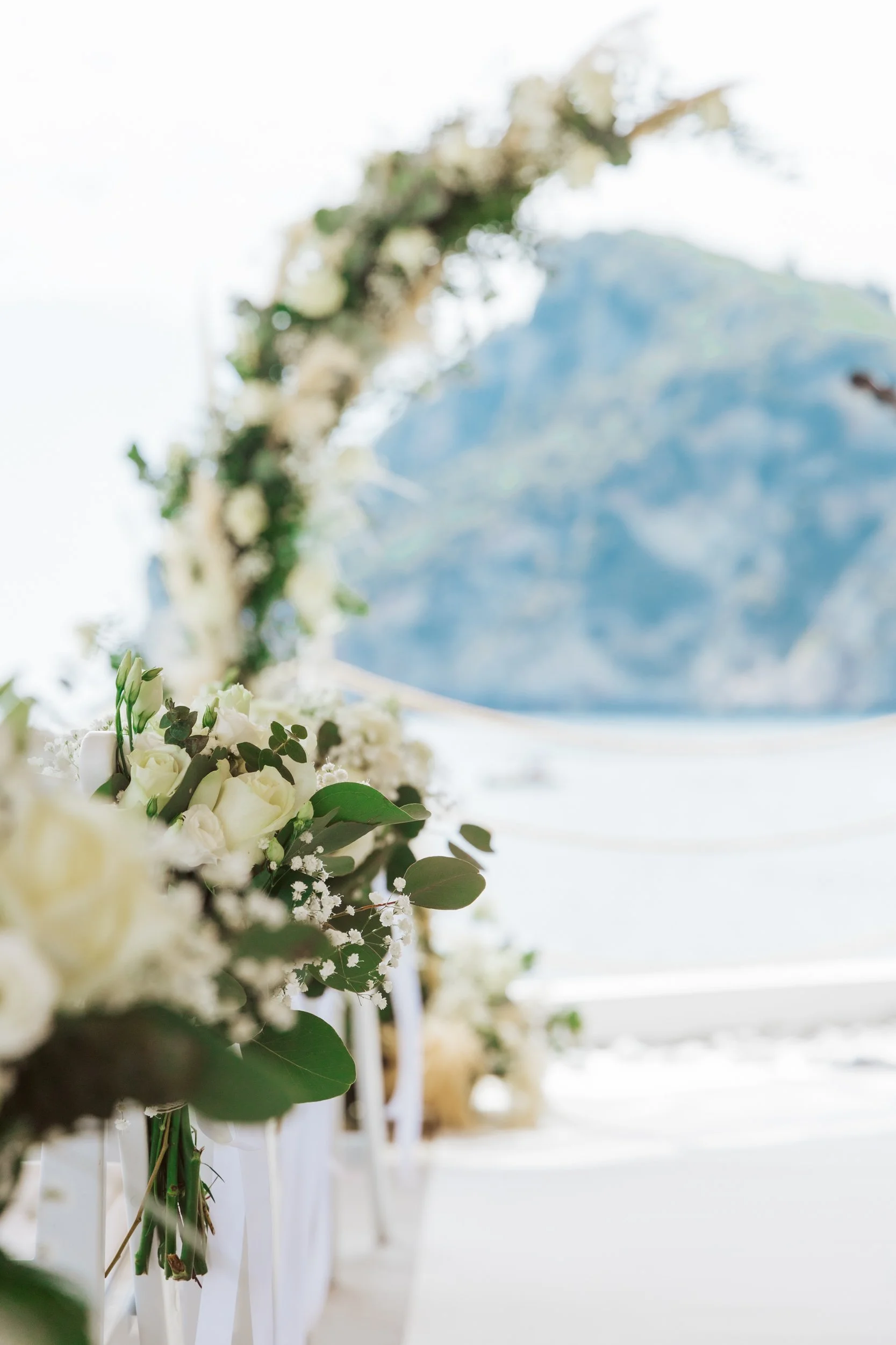 Wedding aisle decorated with white flowers and greenery with a mountain view in the background.