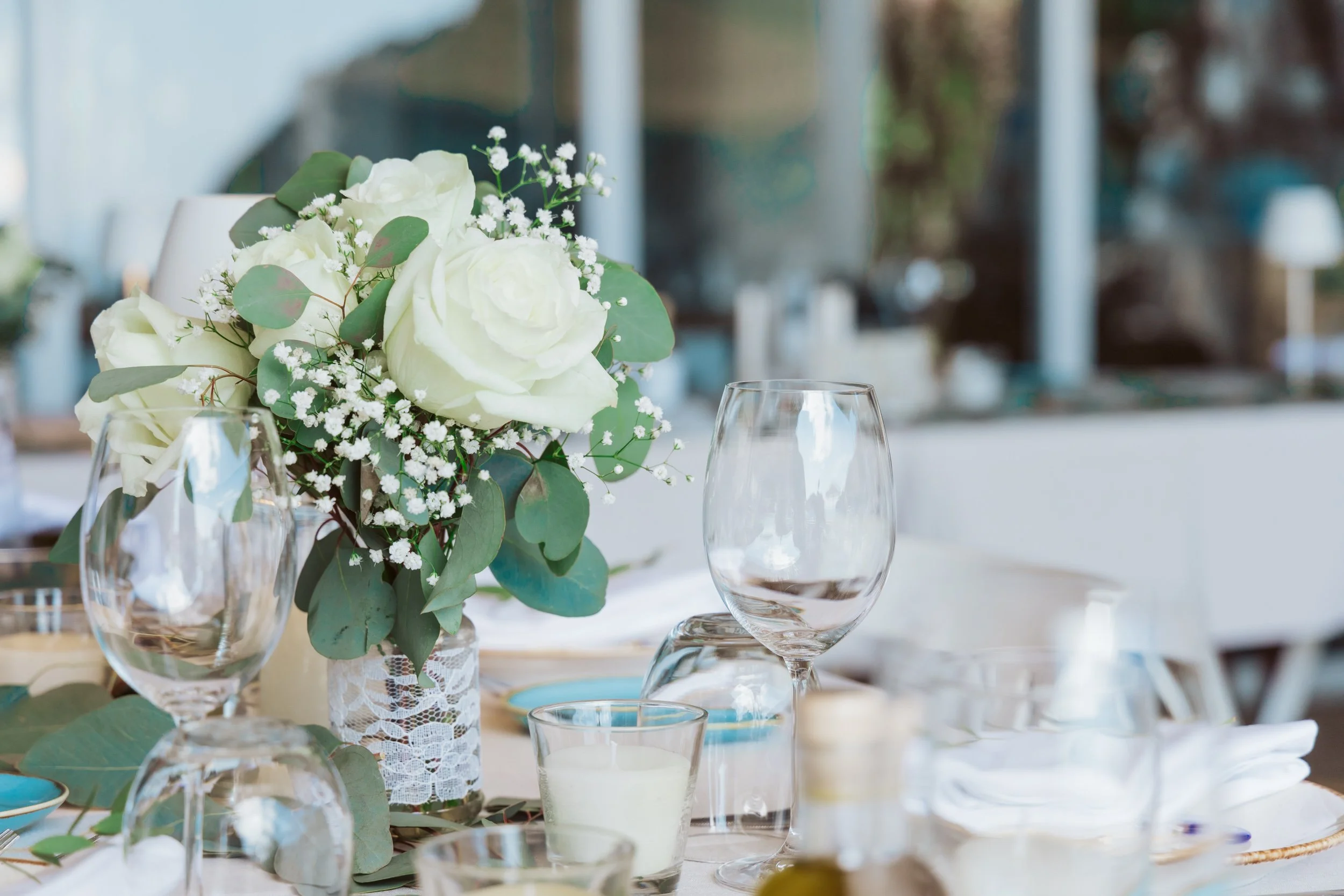 Elegant table setting with a floral centerpiece of white roses and greenery, surrounded by empty wine glasses and candles.