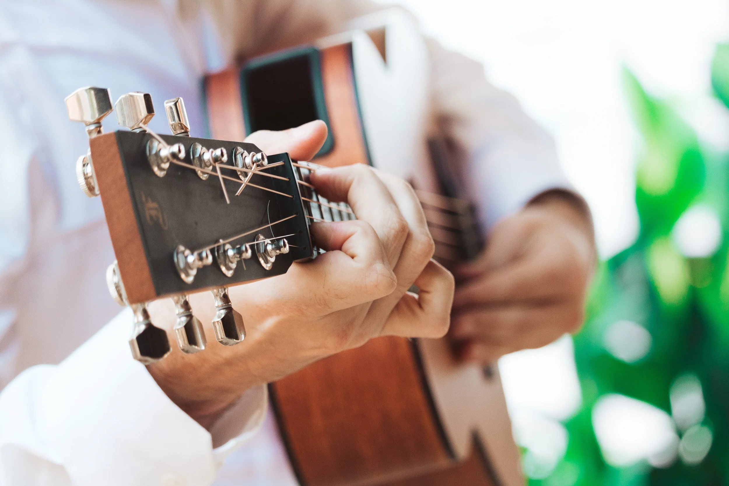 Person playing an acoustic guitar, focusing on their hand pressing the strings on the fretboard.