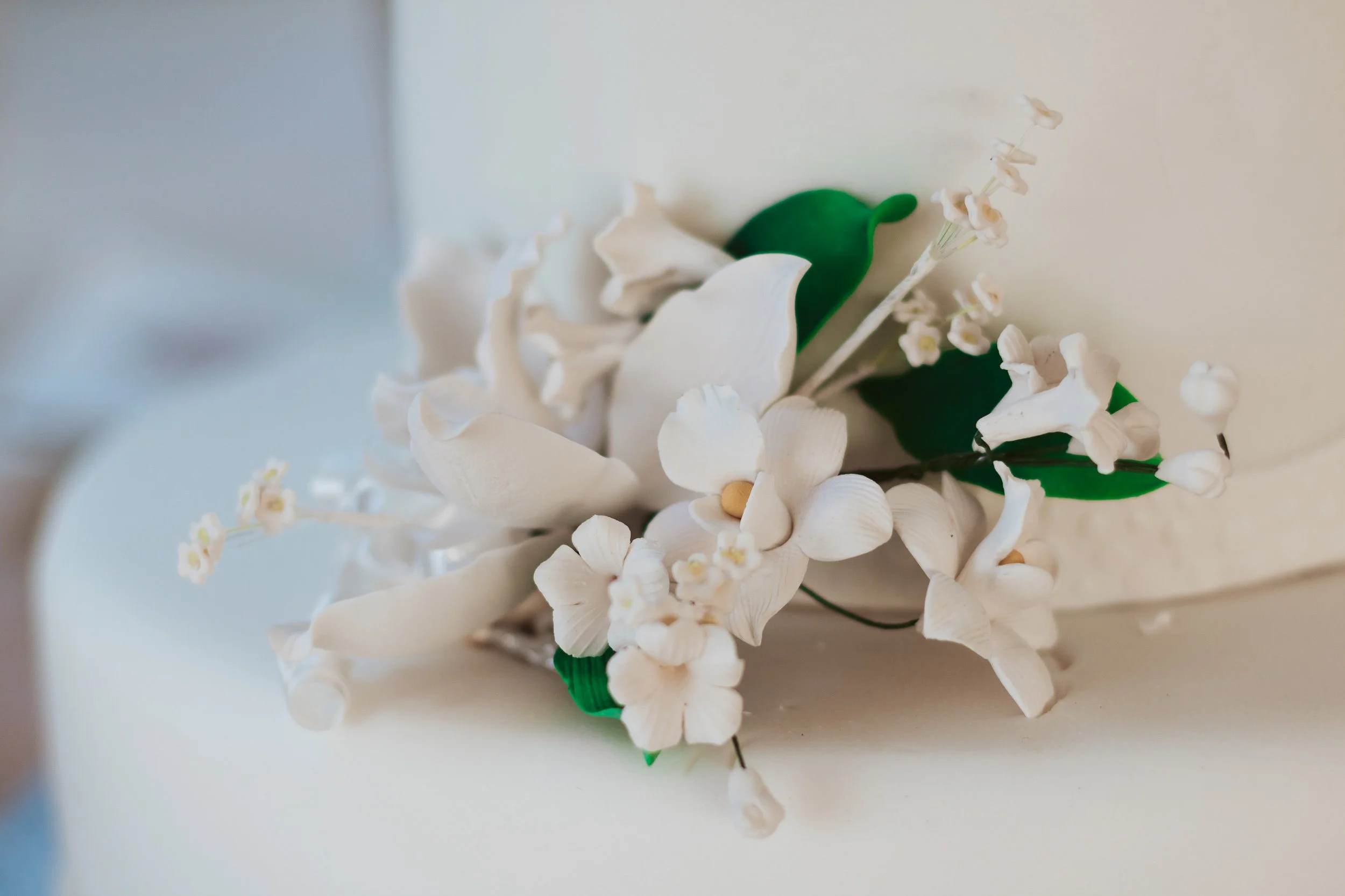 Artificial white flower boutonniere with green leaves and small white buds.