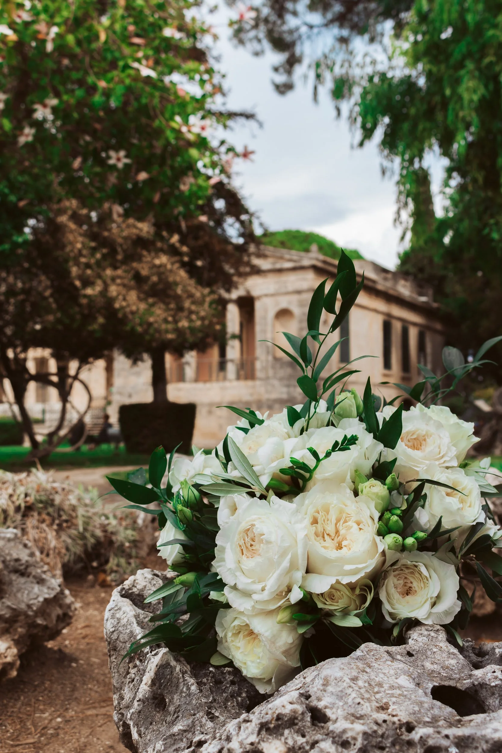 White bouquet of flowers on rocks with an old stone building and trees in the background.