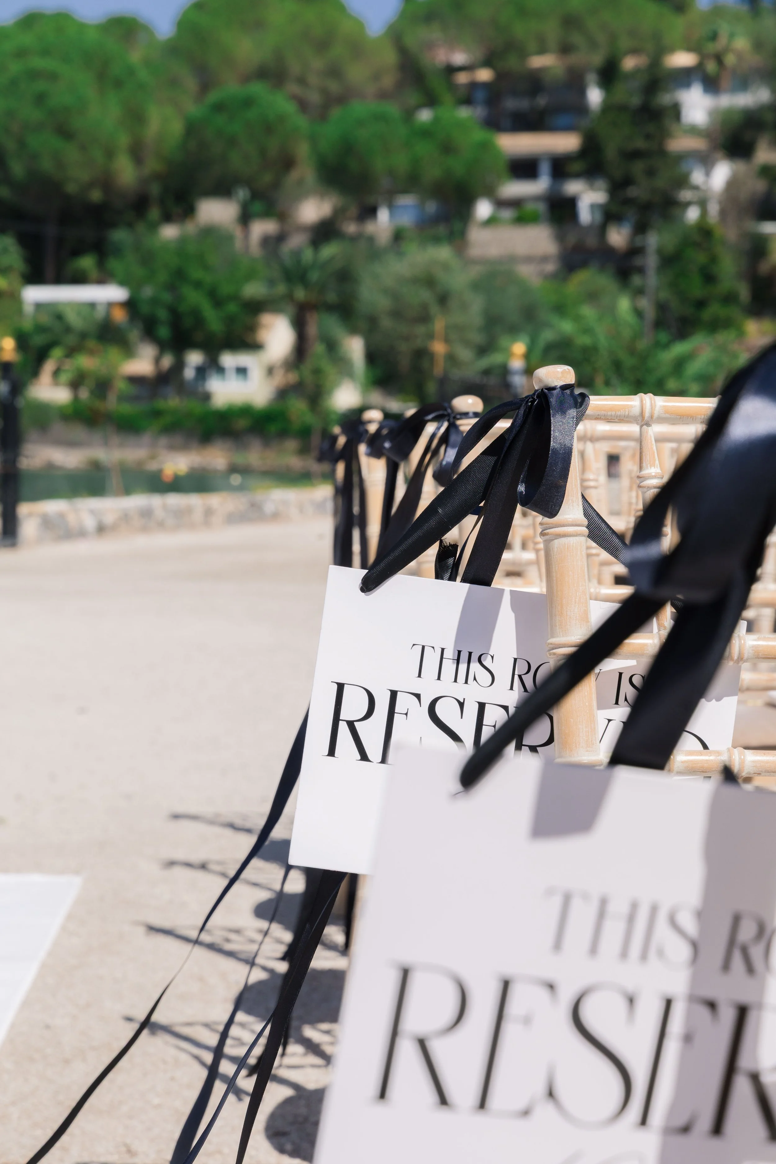 Row of chairs with reserved signs at an outdoor event, with trees and buildings in the background.