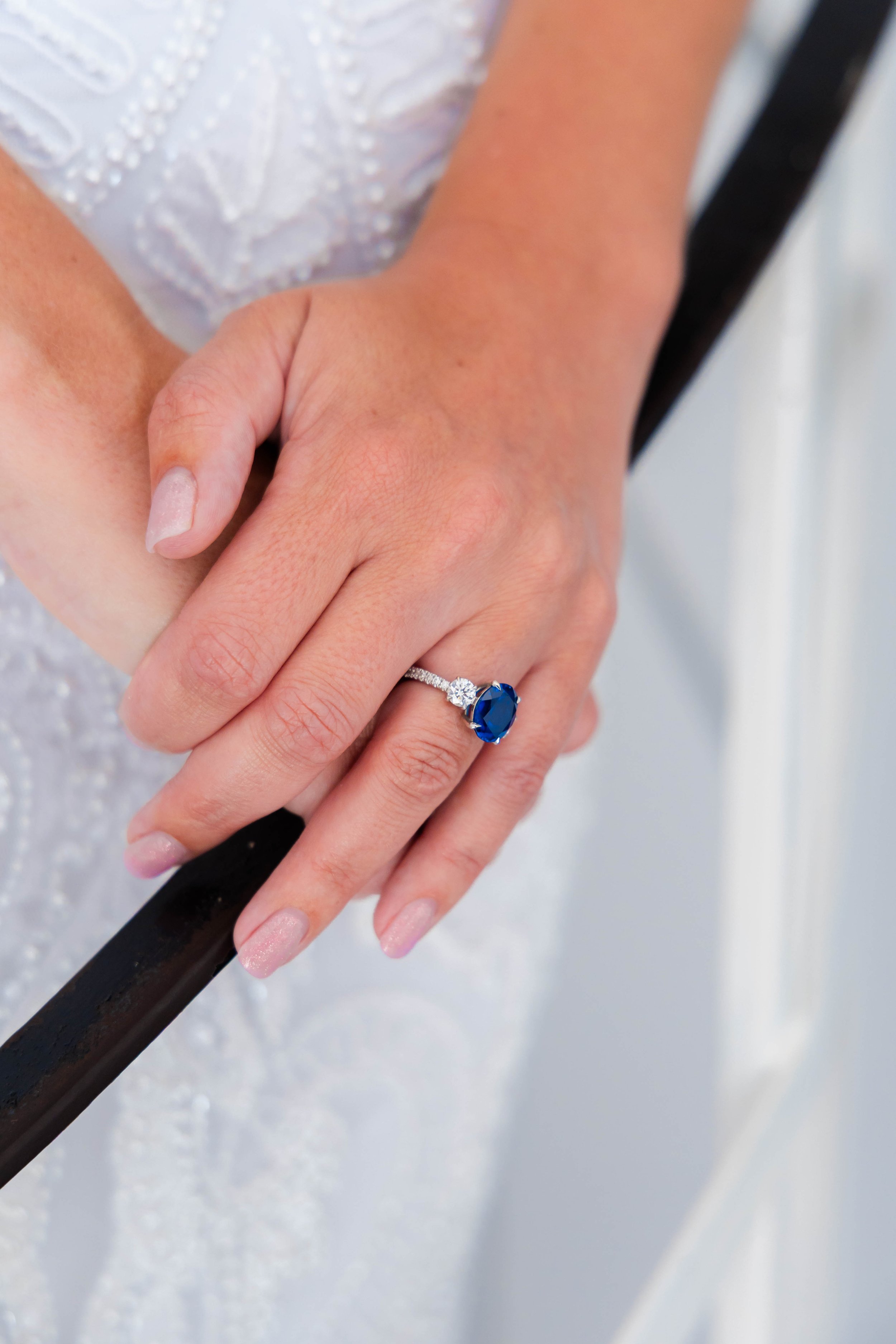 Close-up of hands holding a black baton, showing wedding ring with blue gemstone on the ring finger.