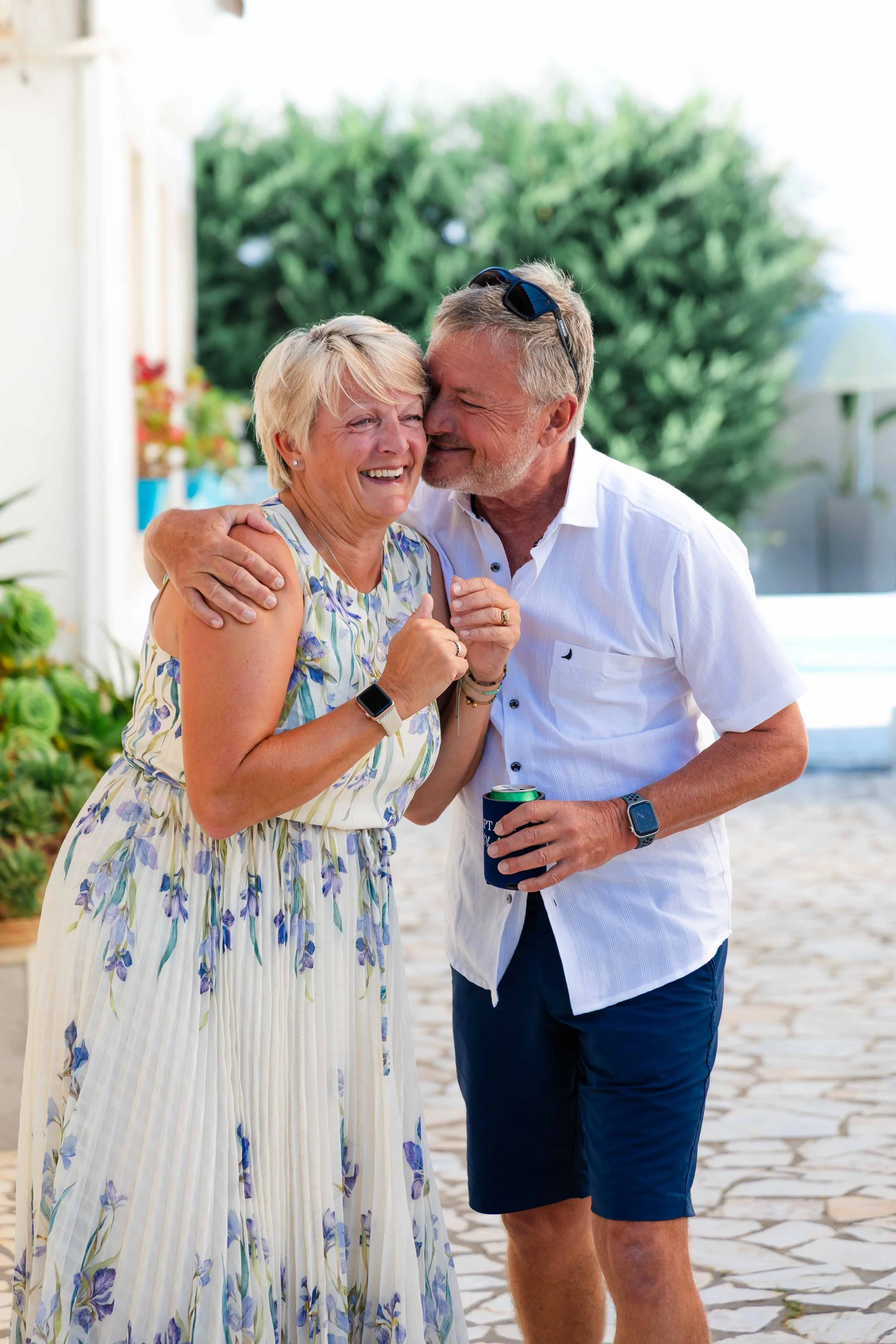 An elderly woman and a middle-aged man sharing a joyful moment outdoors, with the man kissing the woman on the cheek, both smiling and happy.