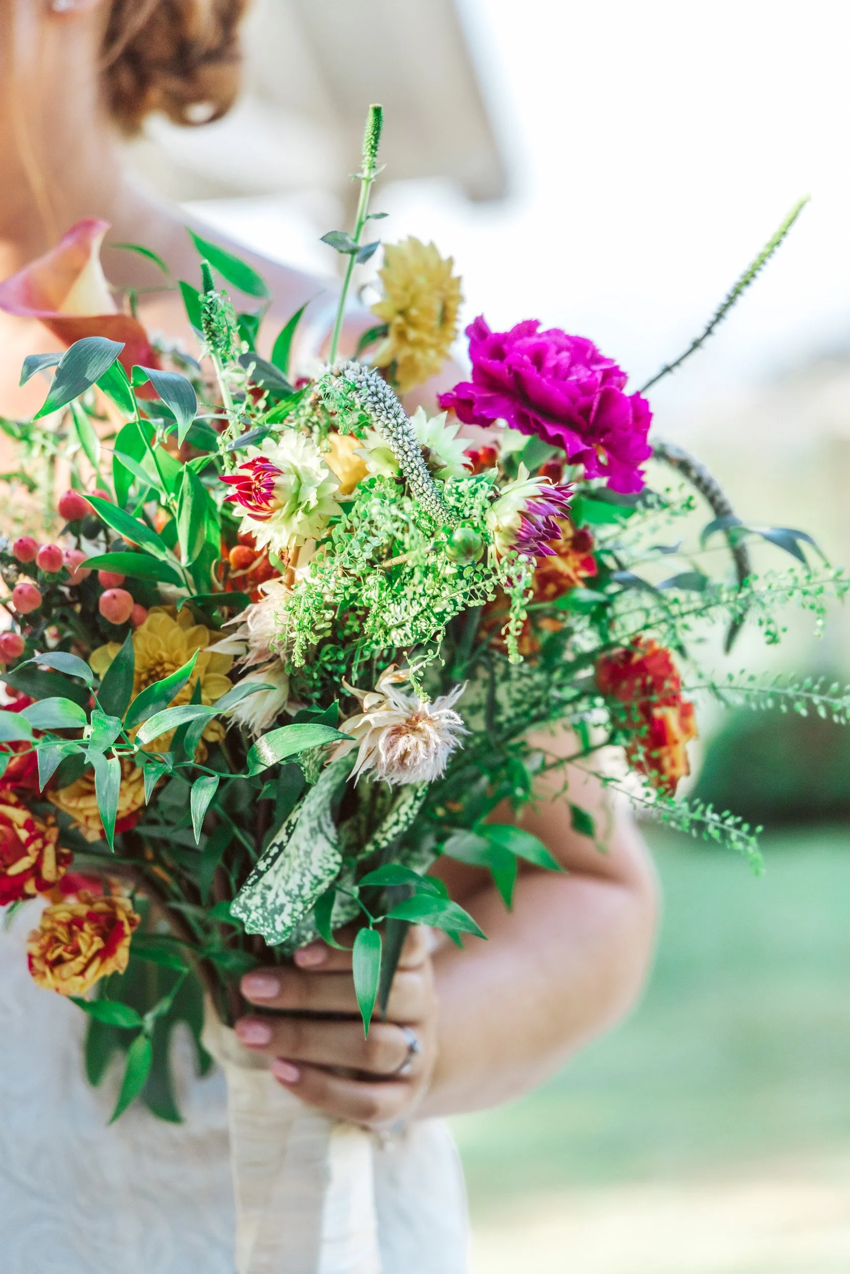Person holding a colorful bouquet of various flowers and greenery outdoors.