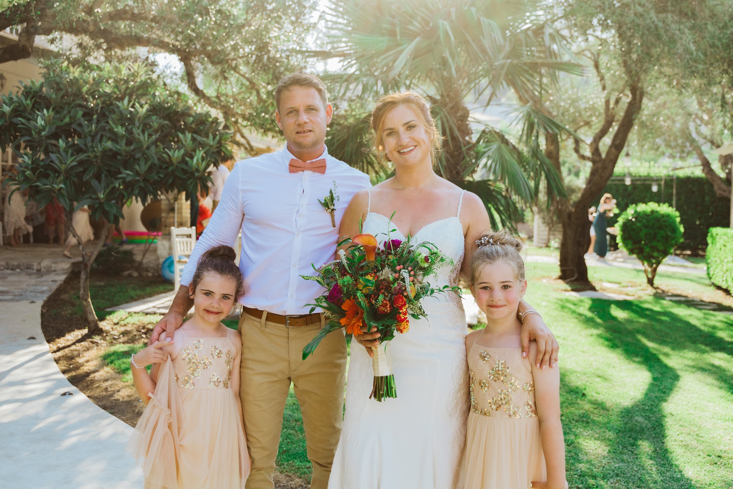 A wedding couple with two young girls in a garden setting.