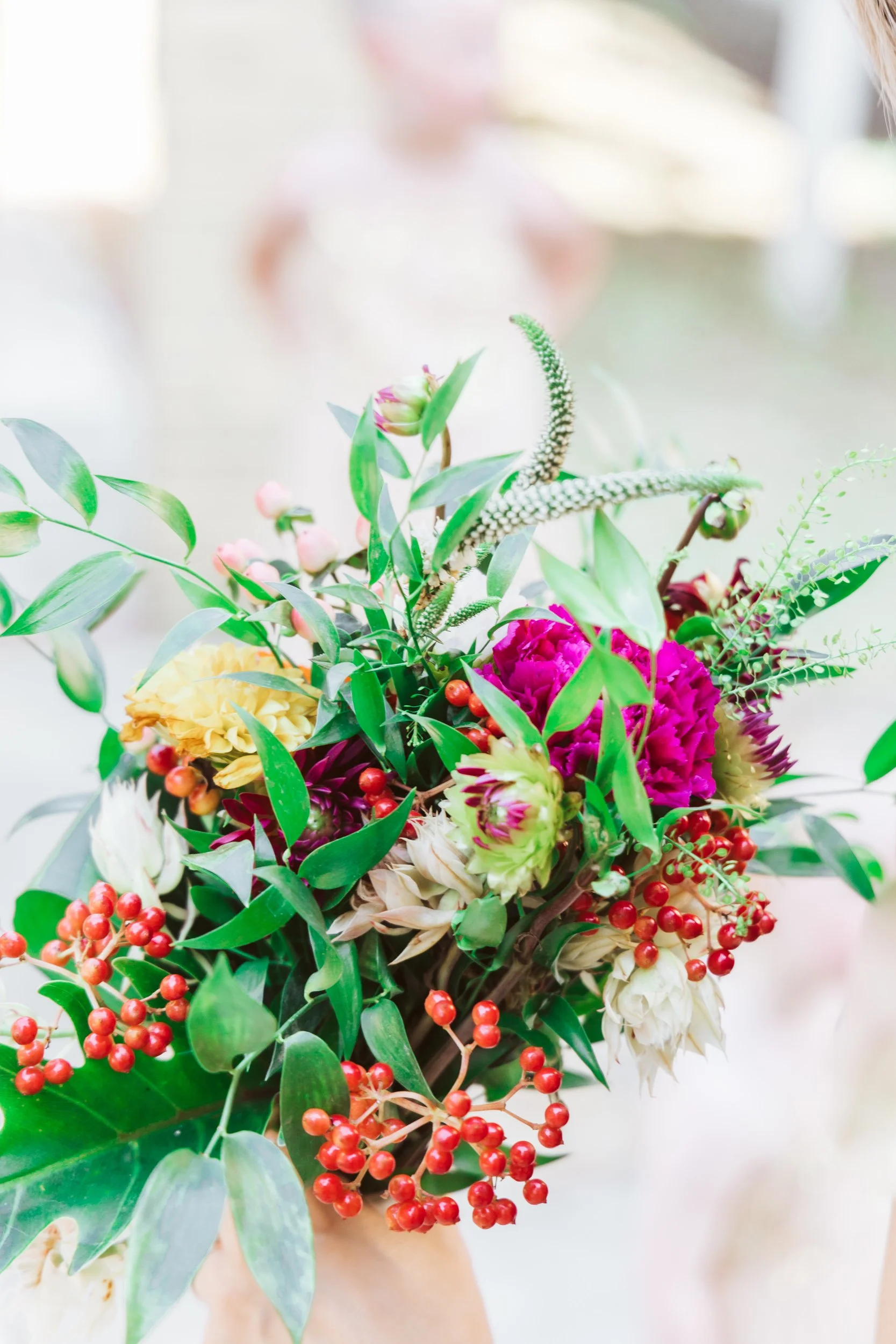 A colorful bouquet of flowers including pink, white, green, and yellow blooms with green foliage and red berries.