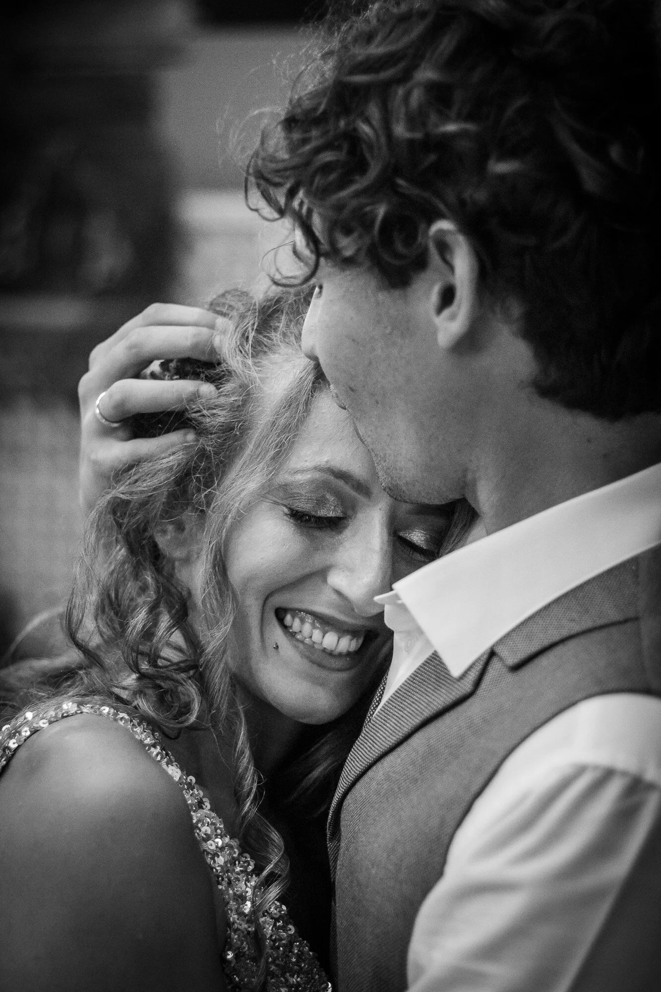 A black-and-white photo of a smiling woman and a man close together, their faces touching, with the woman smiling with closed eyes and the man gently holding her head.