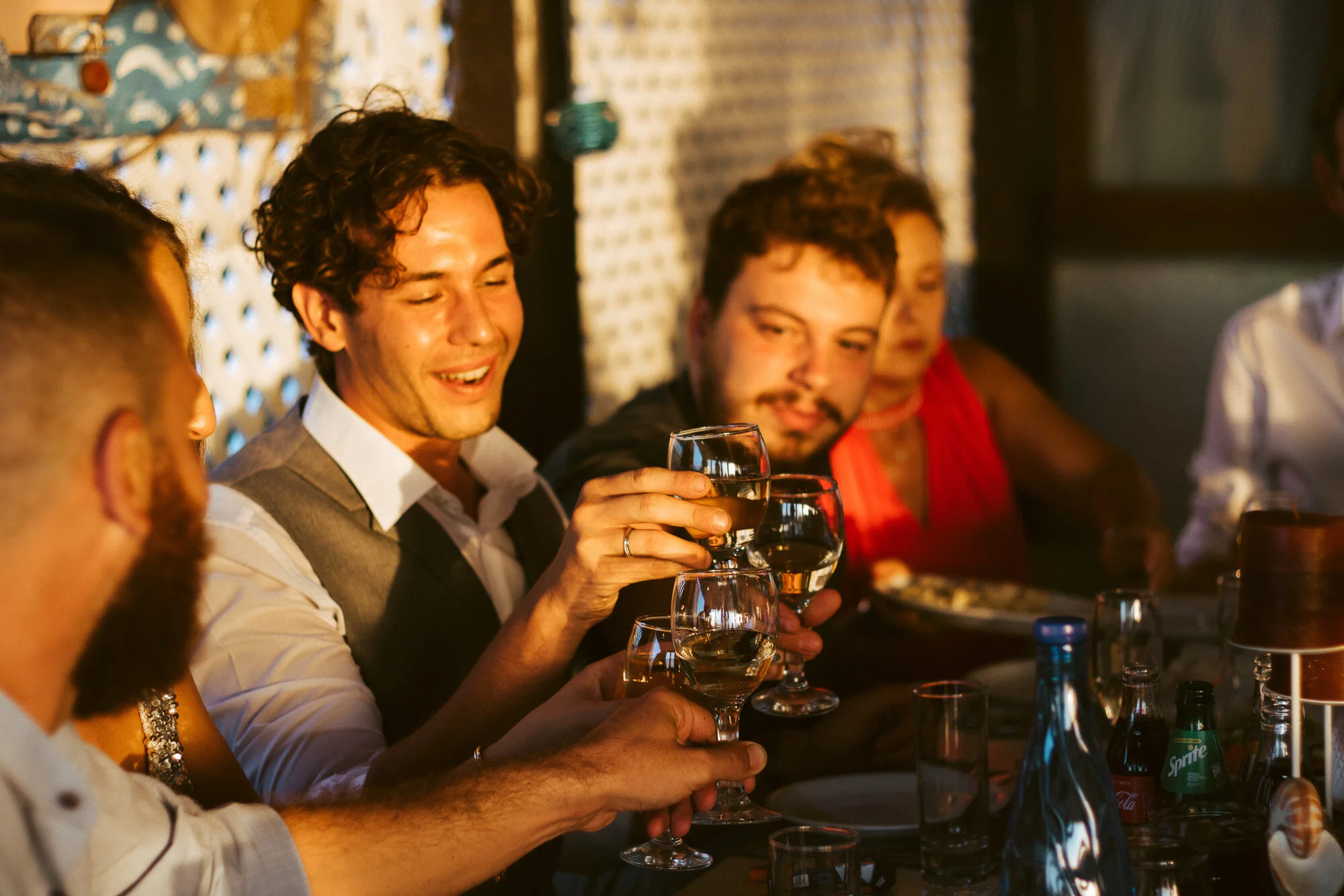 Group of people celebrating at a dinner table, holding glasses of white wine, with a warm, festive atmosphere.