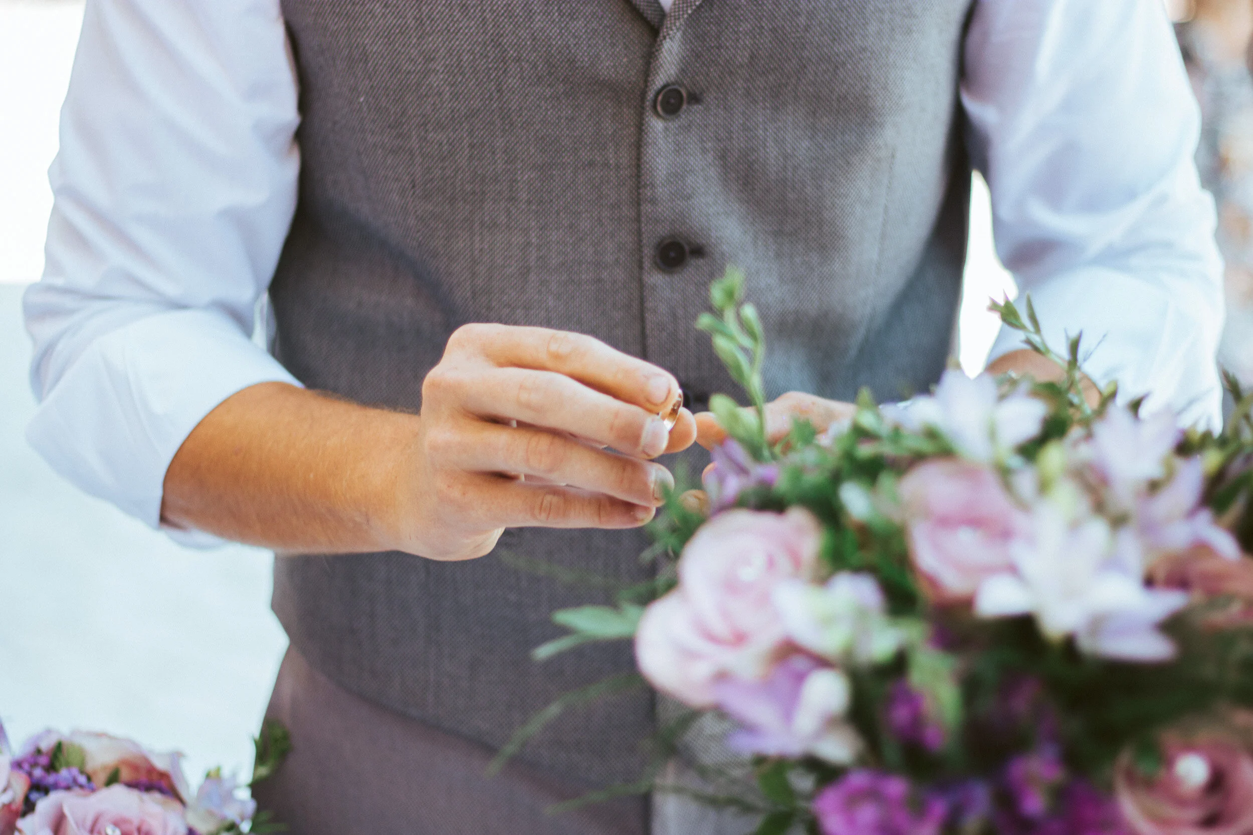 A person arranging a floral bouquet, wearing a gray vest over a white long sleeve shirt, with focus on hands and flowers.