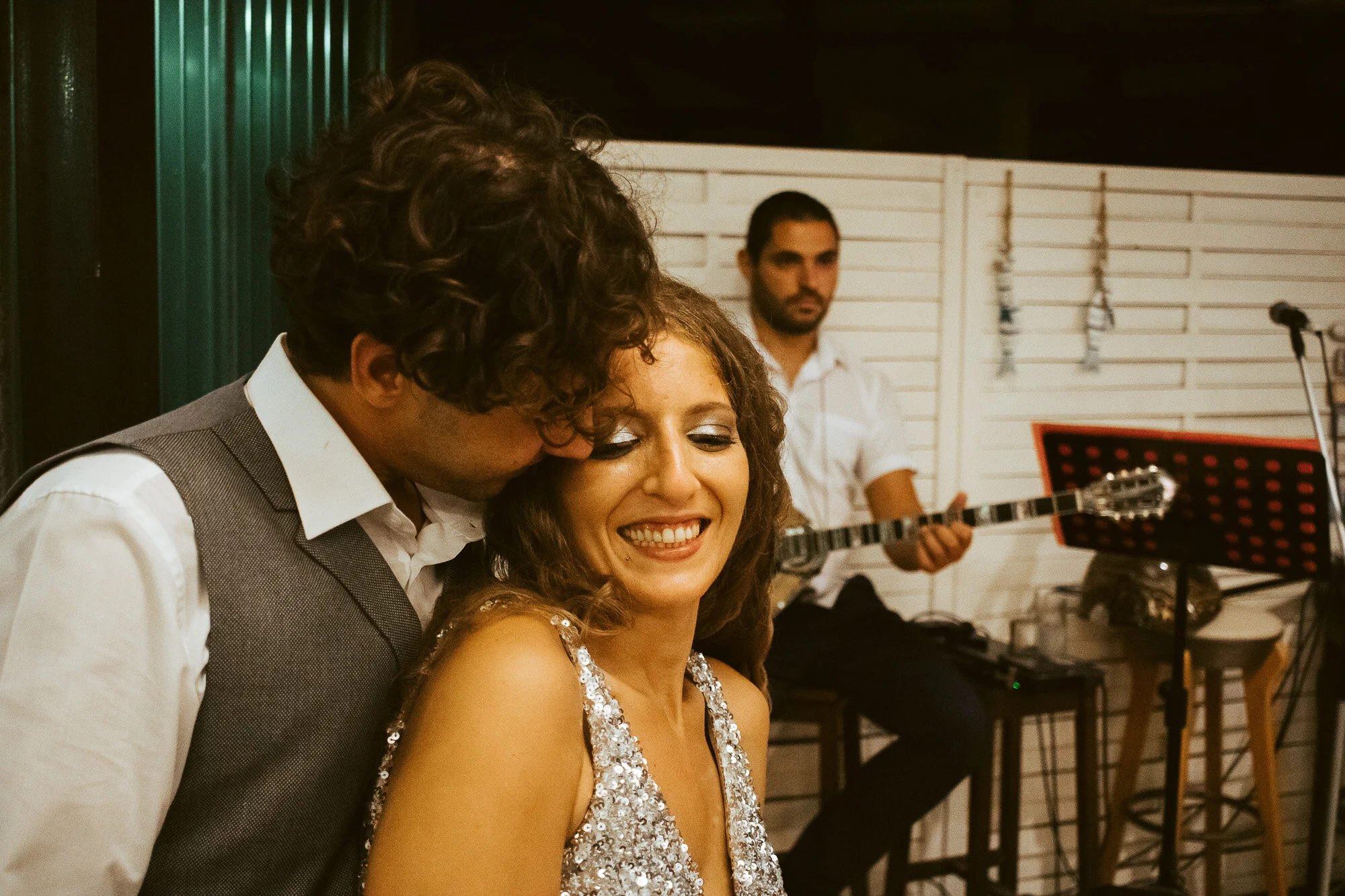 Couple at a celebration with a musician playing guitar in the background.