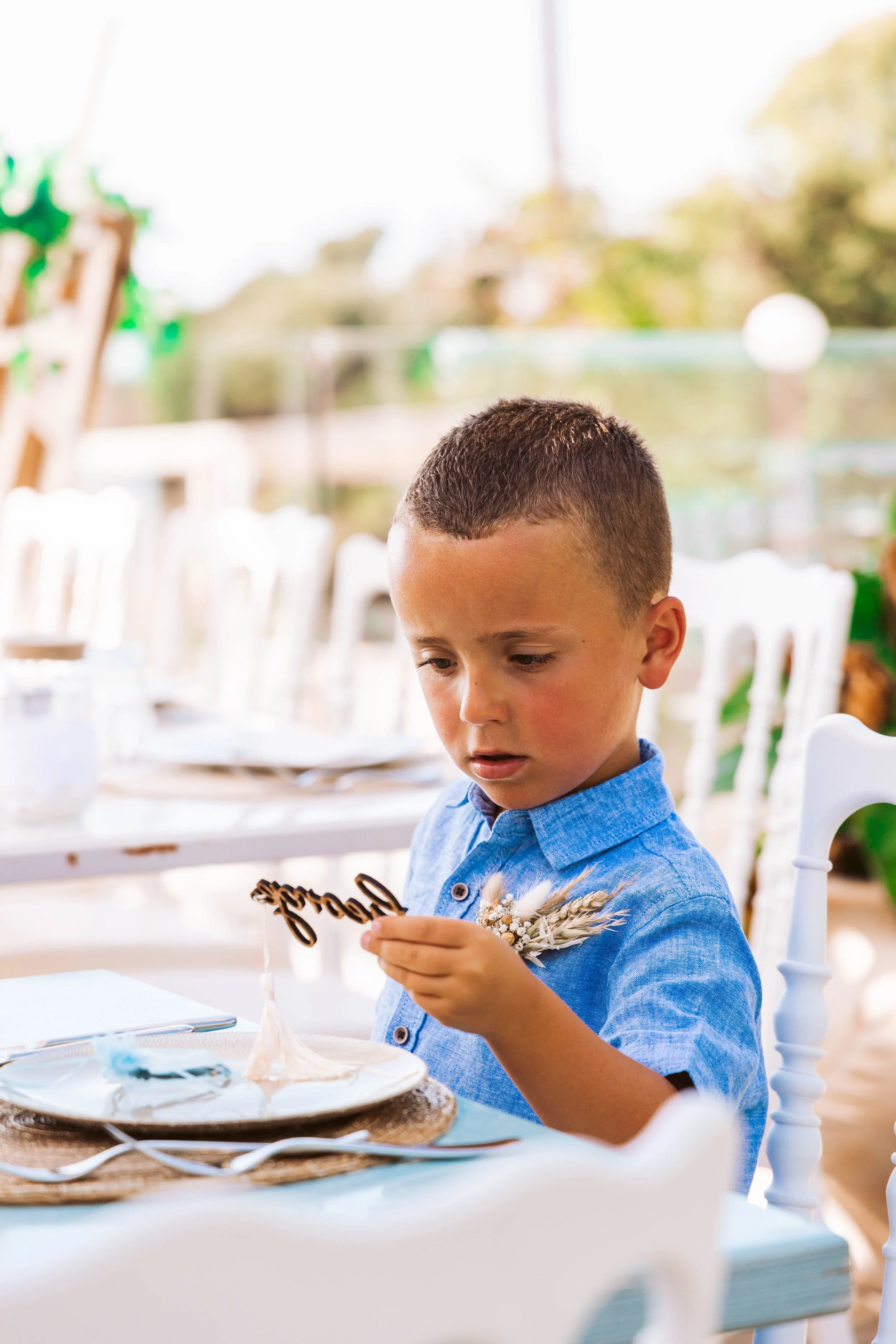 A young boy in a blue shirt looks at a small decorative item on a table at an outdoor event.