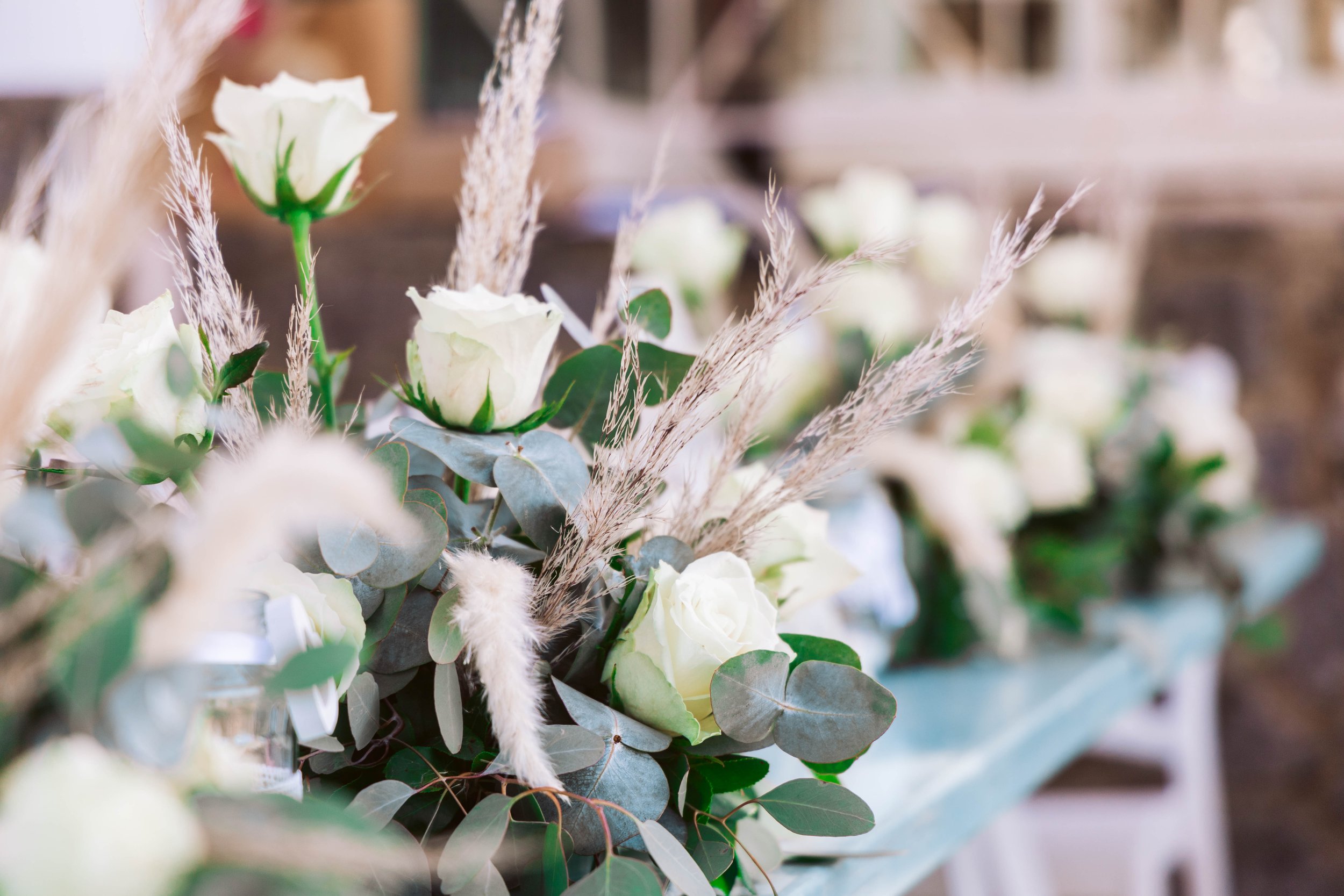 Close-up of white roses and greenery with dried pampas grass in a floral arrangement.