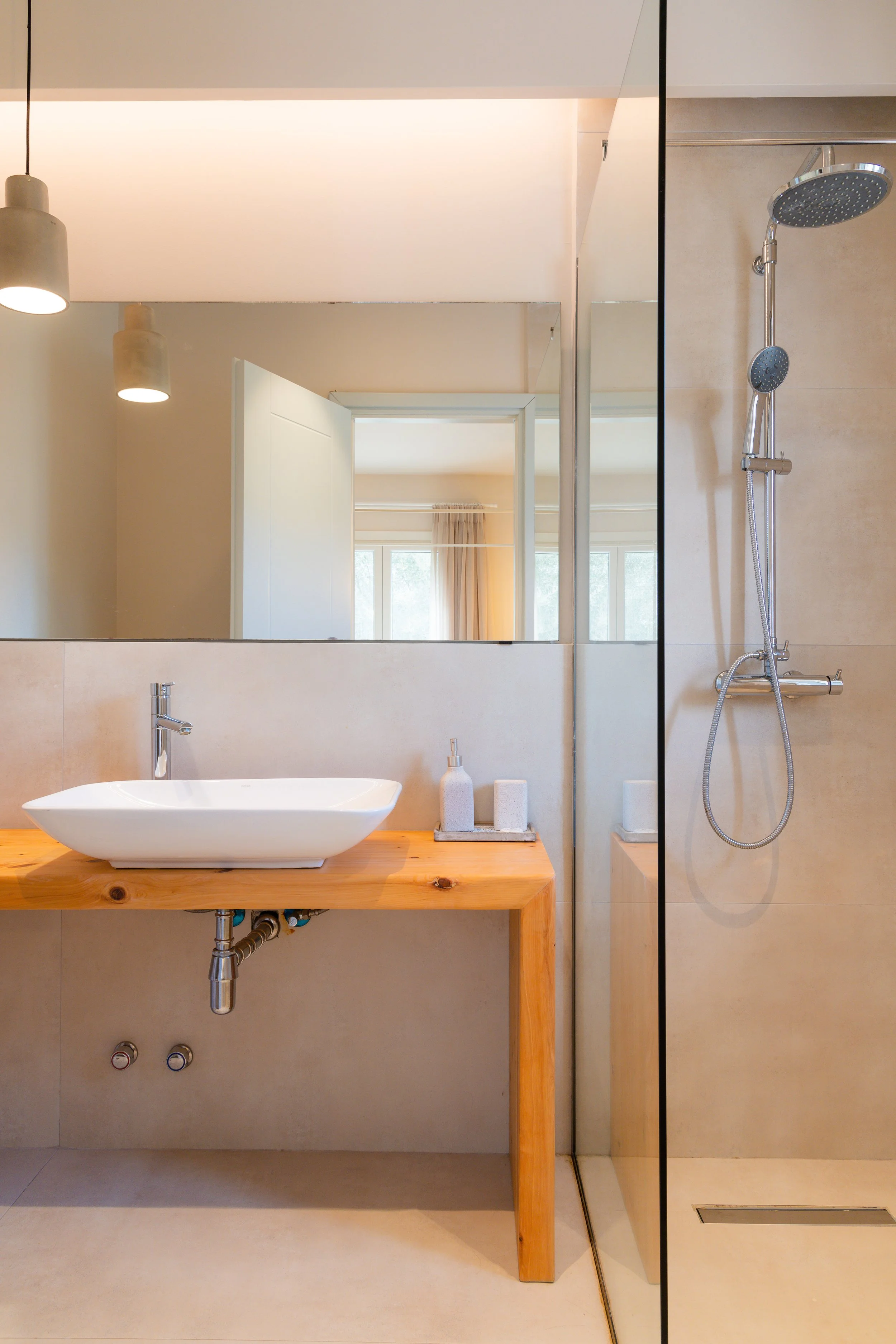 Modern bathroom with a wooden vanity, vessel sink, large mirror, and a walk-in shower with a rainfall showerhead.