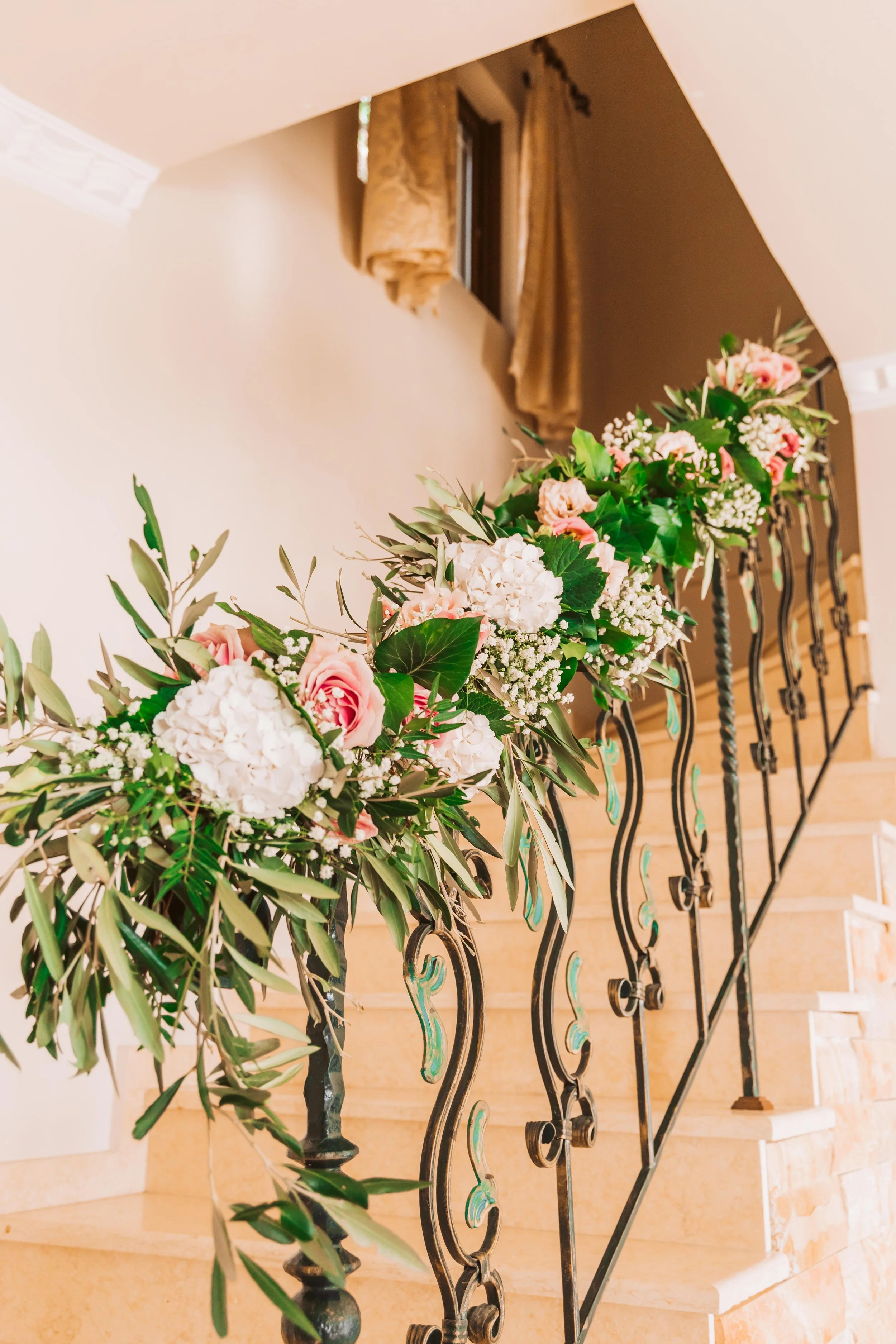 Decorative floral arrangement on a staircase railing with pink roses, white hydrangeas, and greenery.