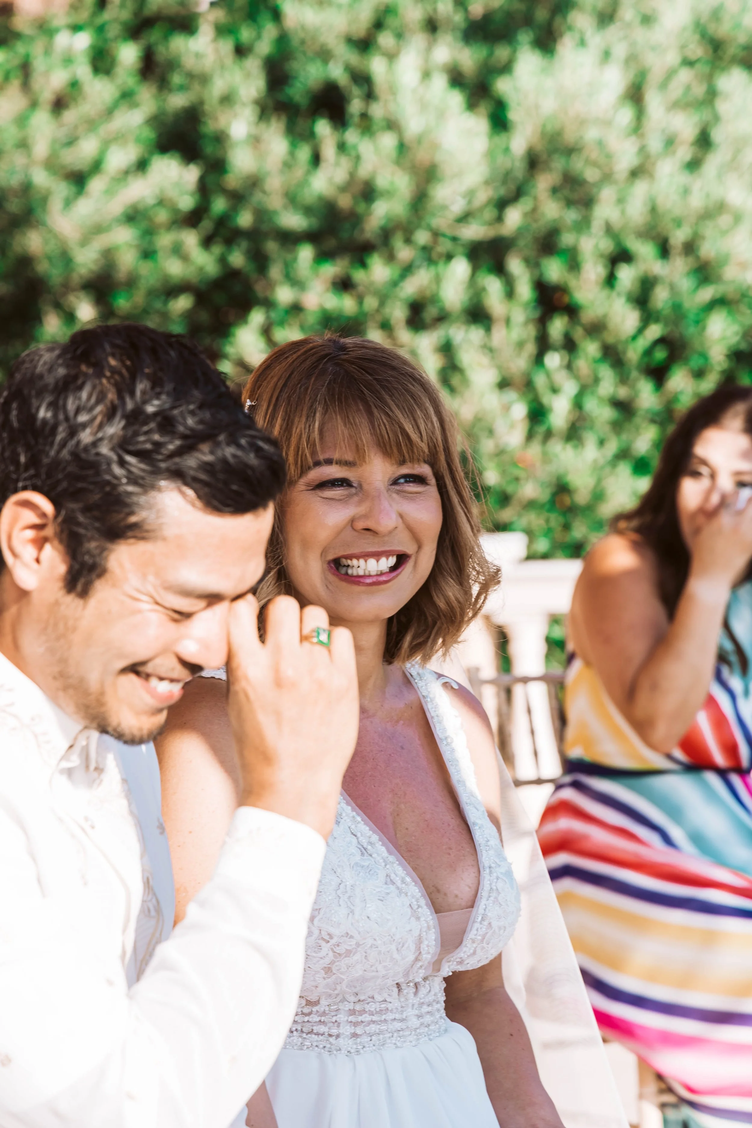 People enjoying a picnic or outdoor gathering, smiling and laughing with a green, leafy background.
