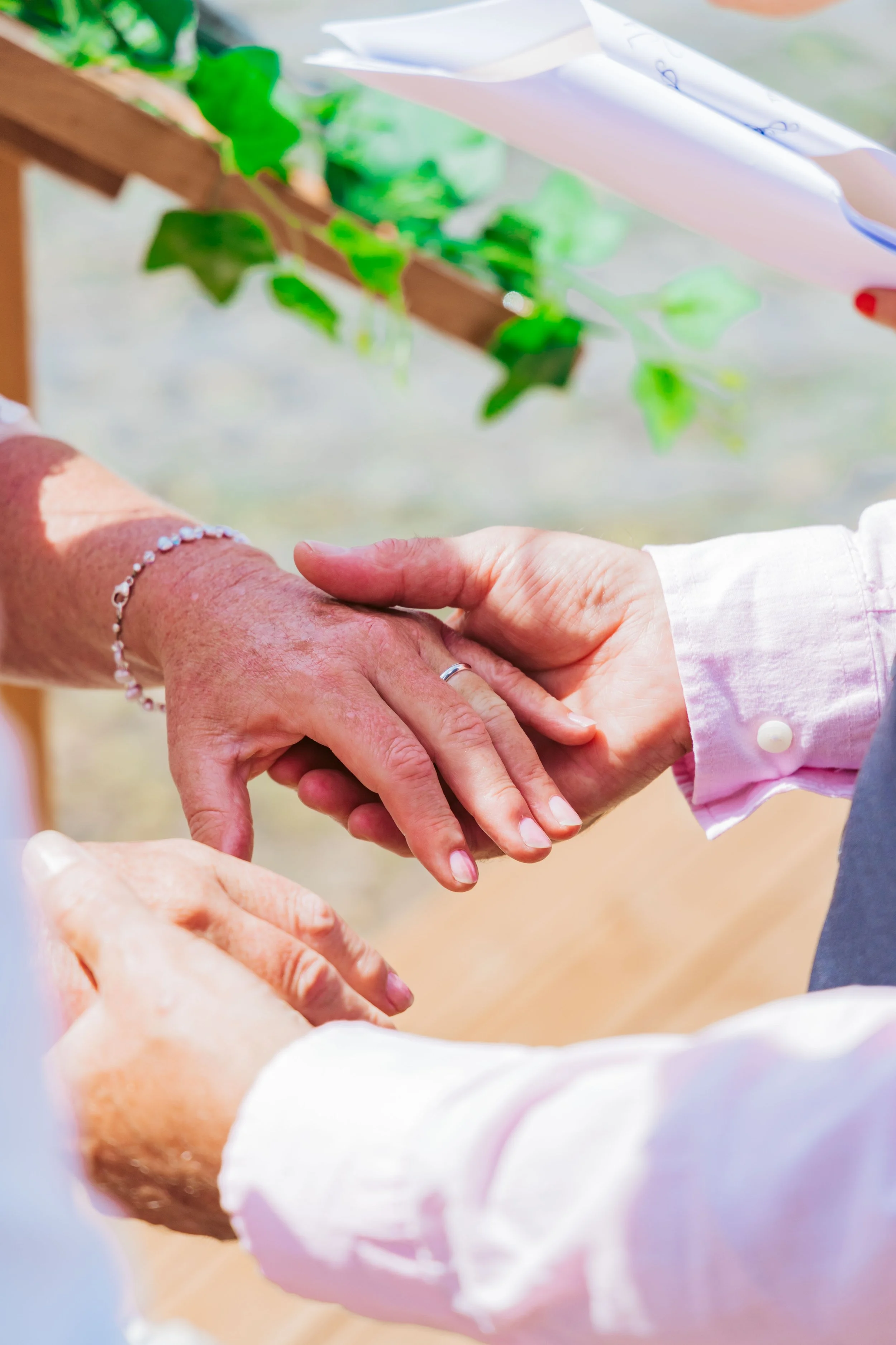 A man and woman holding hands during a wedding ceremony, with the bride wearing a bracelet and the man in a suit with a white shirt.