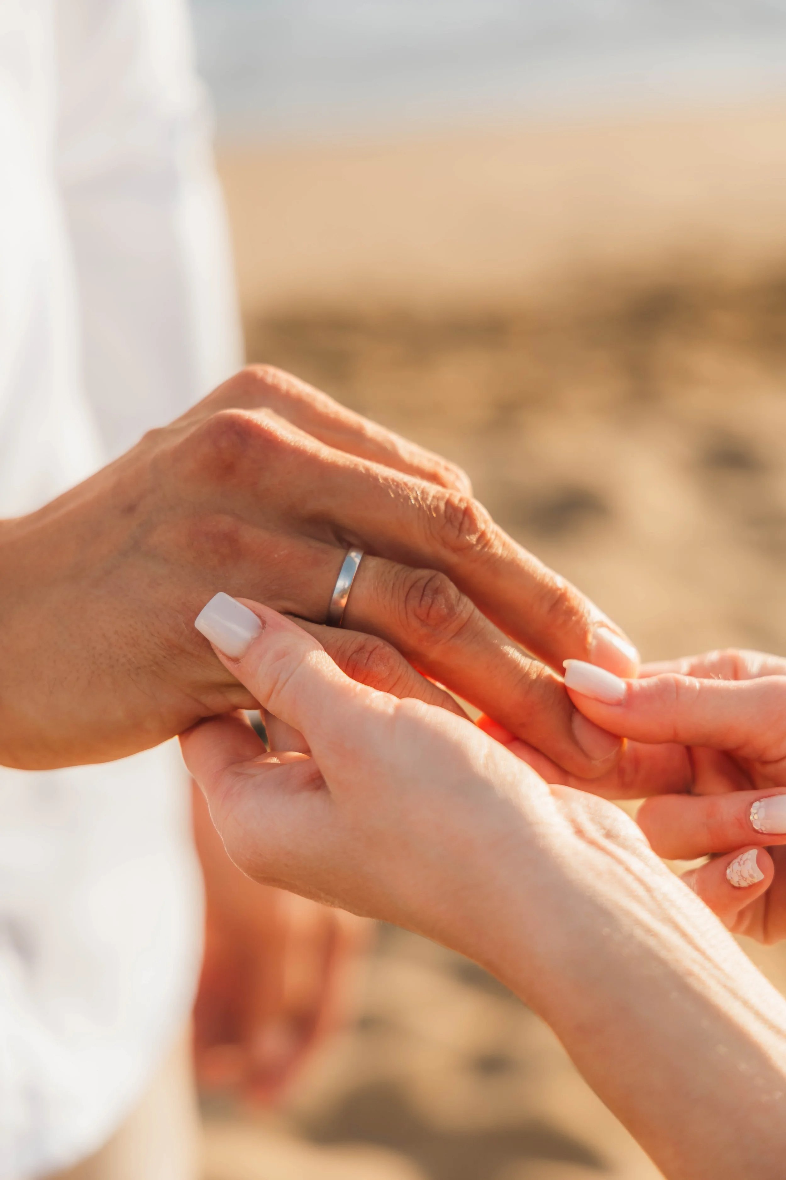 Close-up of hands exchanging rings outdoors during sunset.