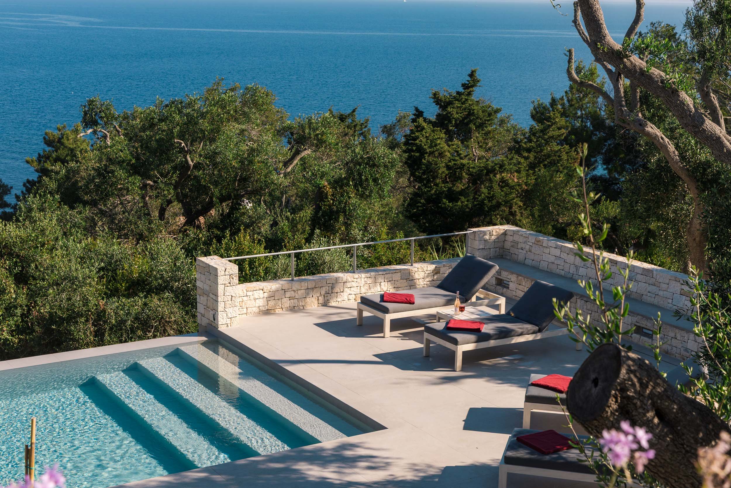 A poolside area with lounge chairs, red towels, and an ocean view in the background.