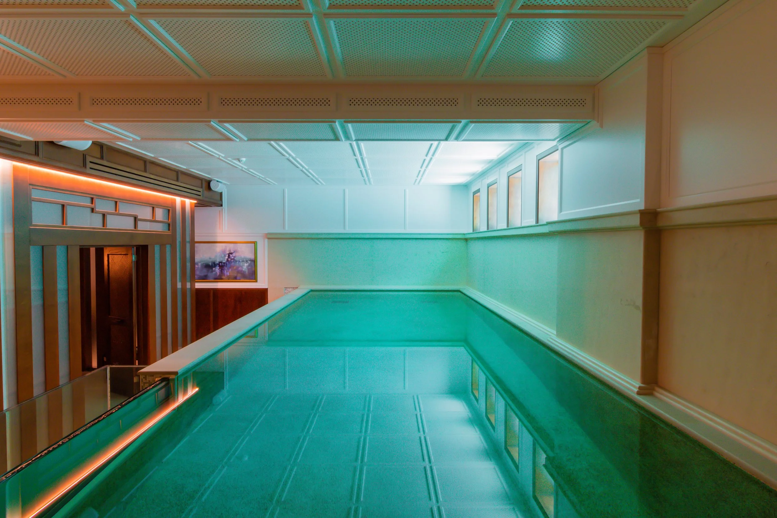 Indoor swimming pool with vibrant lighting, interior design details, and windows on one side.