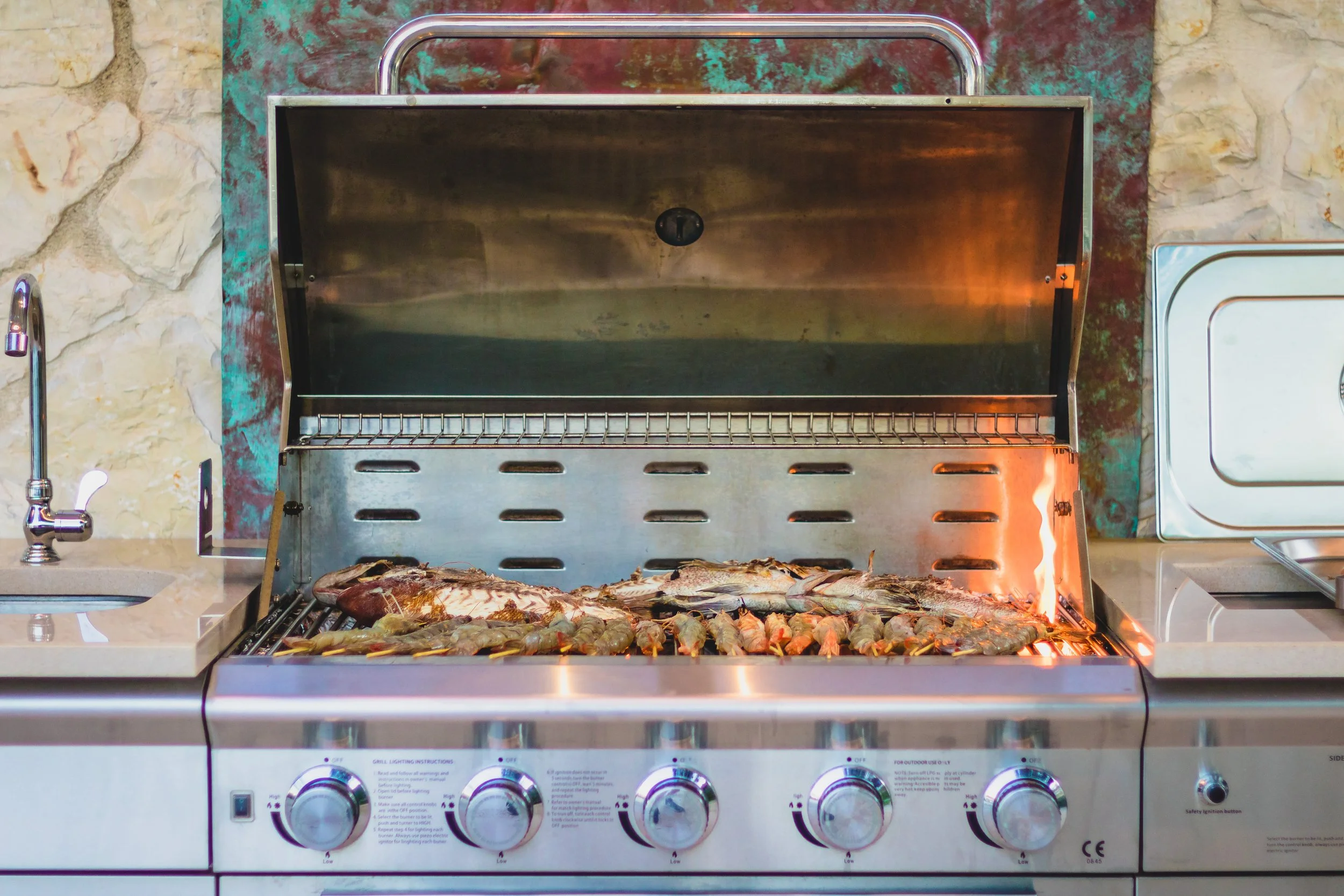 Stainless steel outdoor grill with seafood, including fish and shrimp, cooking on it.