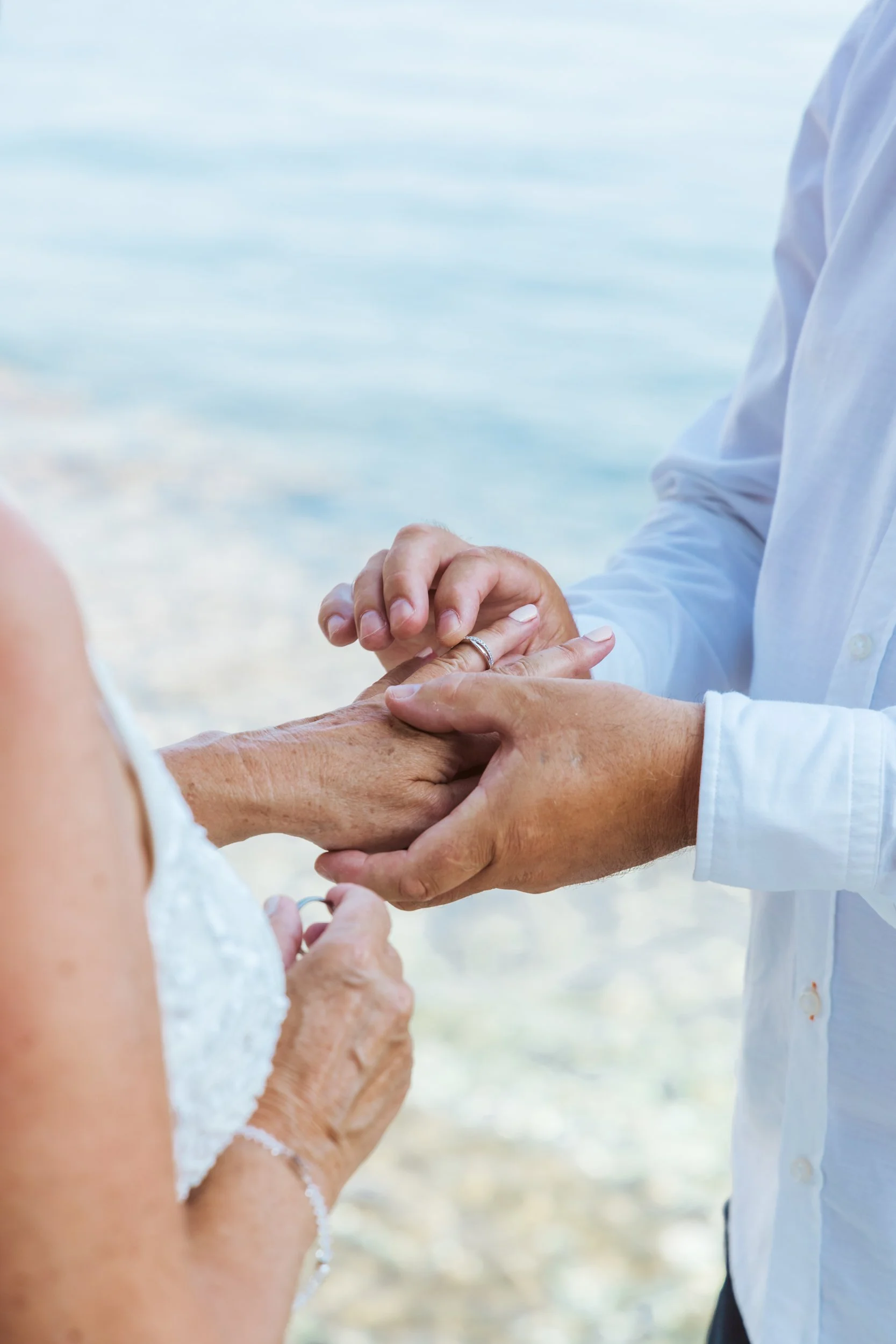 A person holding an elderly person's hand during a wedding ceremony by the beach.