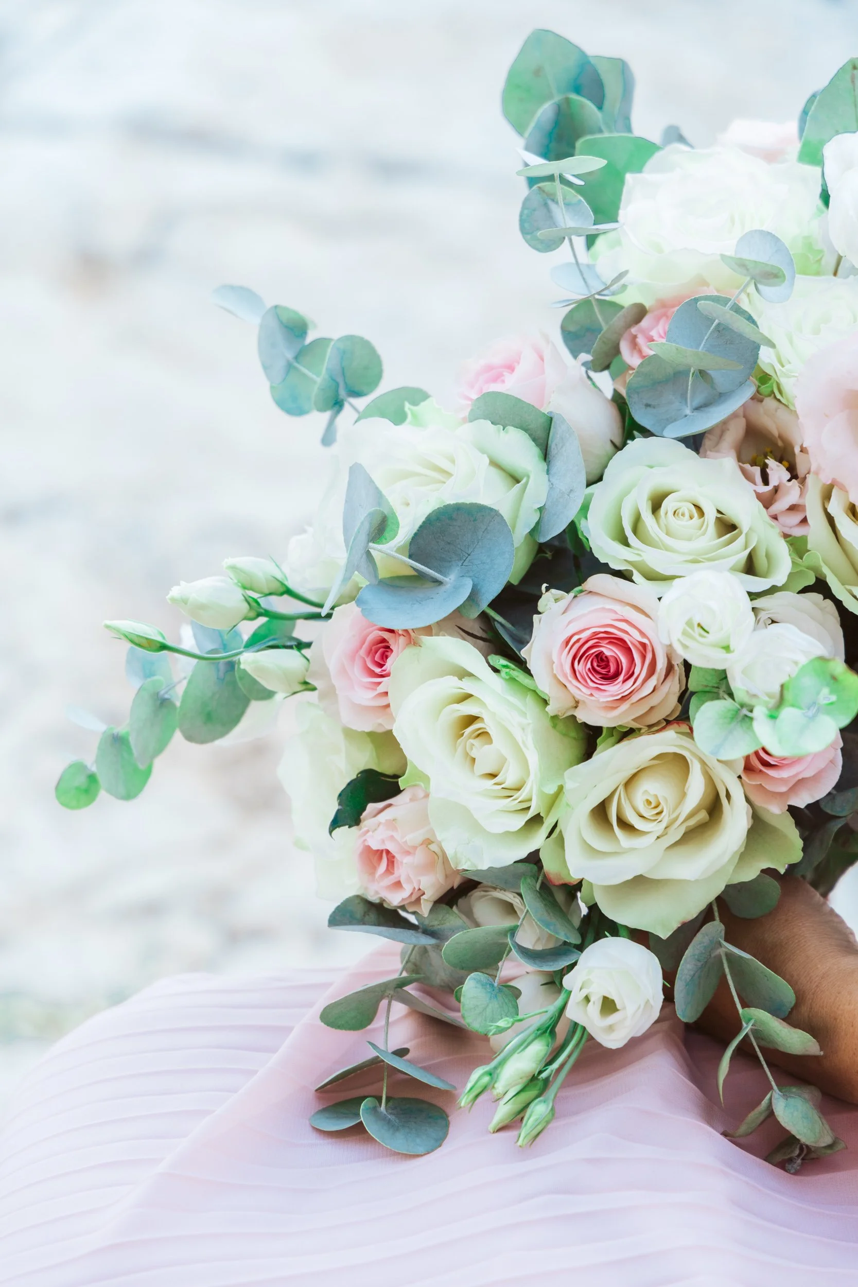Bouquet of white and pink roses with eucalyptus leaves held over a pink pleated fabric.