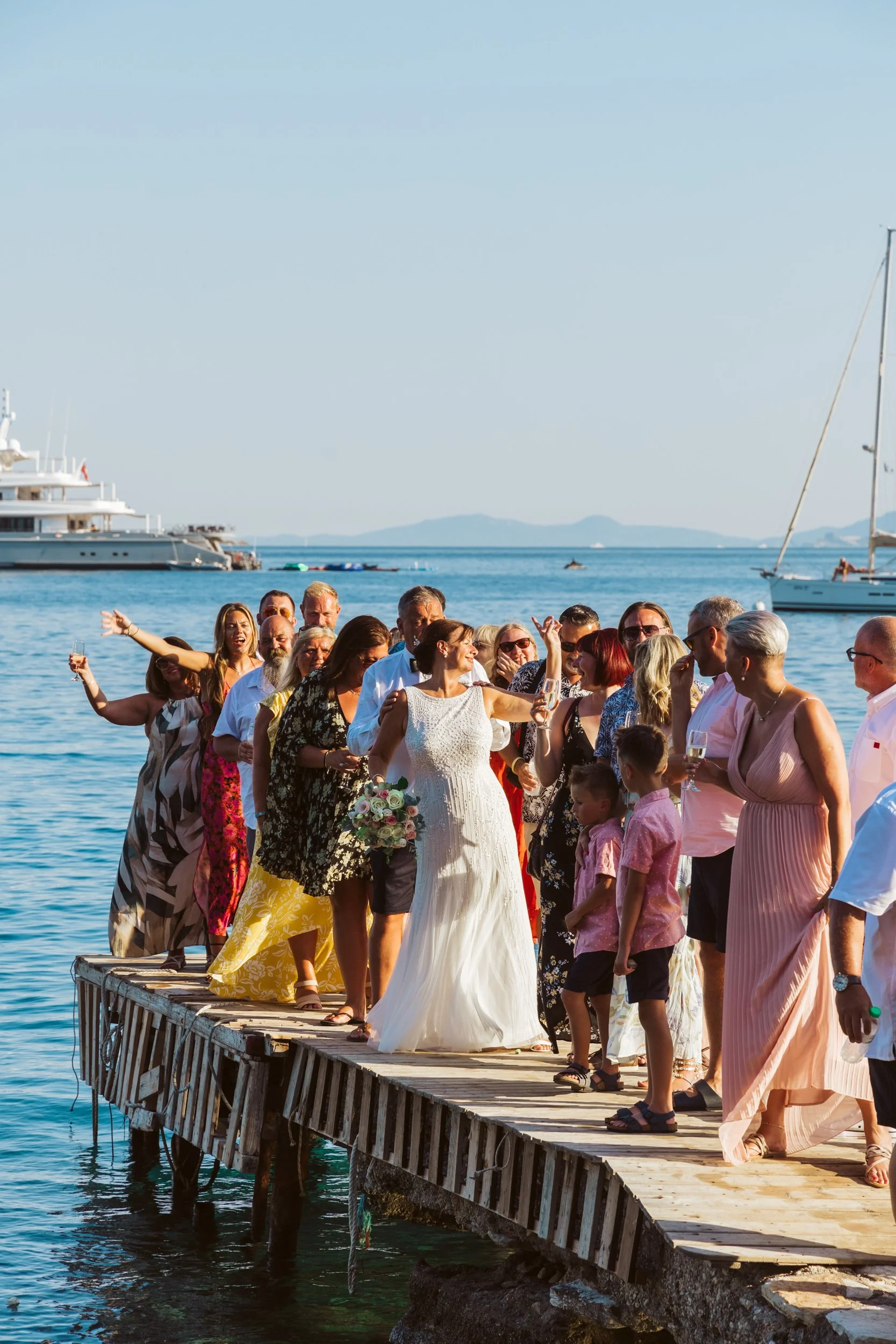 Group of people celebrating on a dock by the water, with boats and yachts in the background on a sunny day.