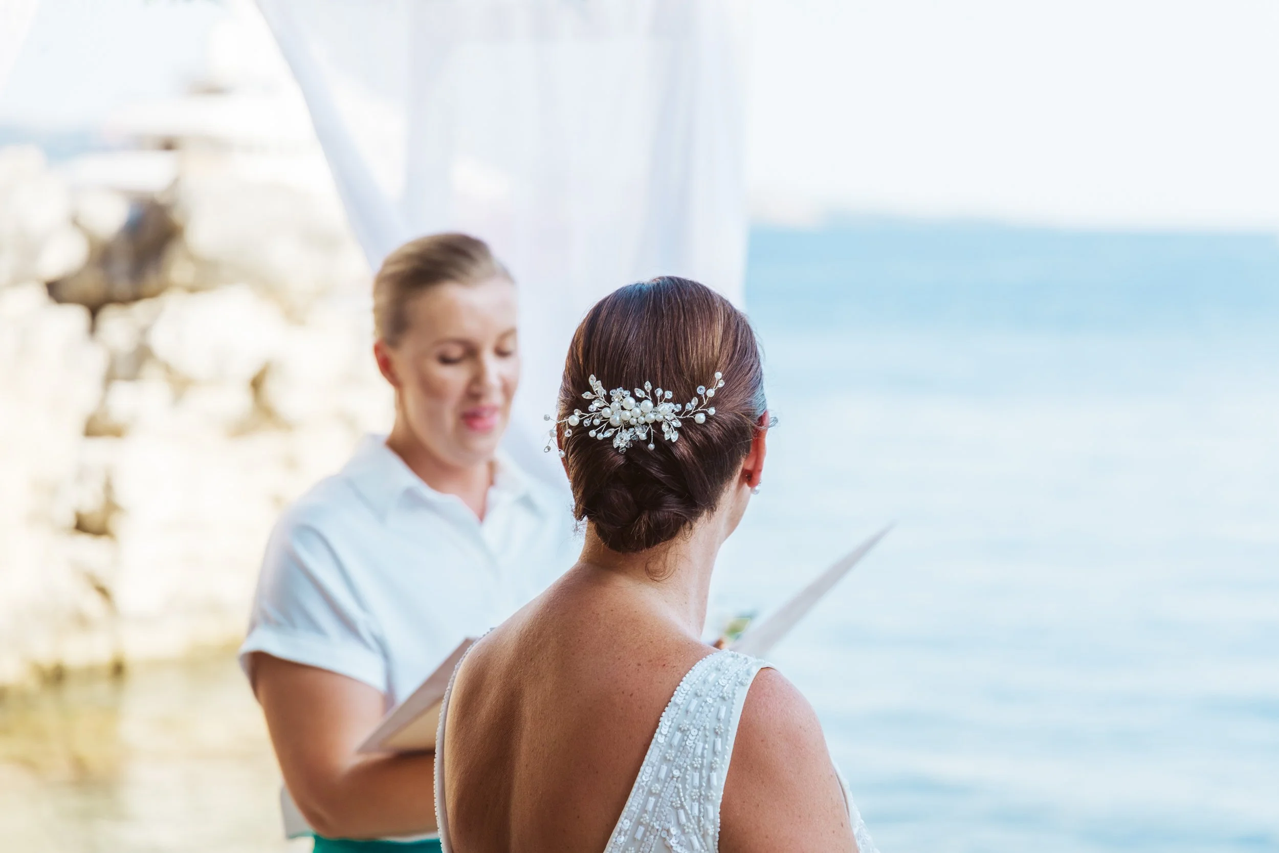 A woman in a wedding dress getting married by the water, with an officiant reading vows during a seaside wedding ceremony.